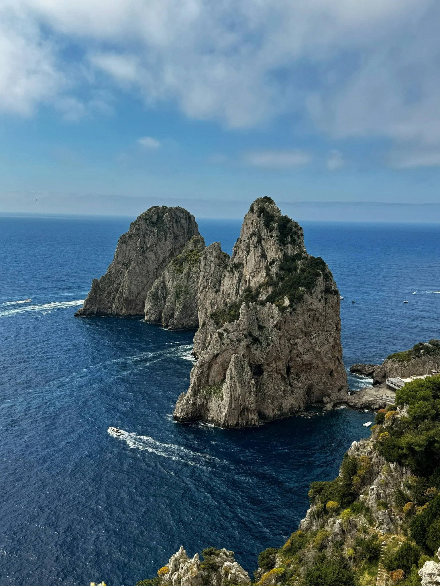 Cliffs rising from the ocean near a coastal landscape with a partly cloudy sky. Capri, Amalfi Coast, Italy