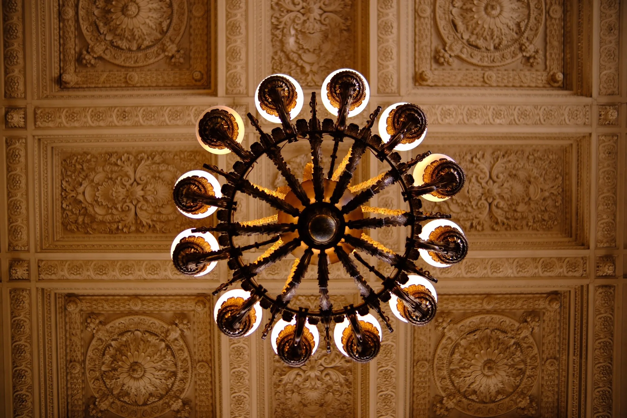 Elegant chandelier with multiple light bulbs hanging from an ornate ceiling with intricate decorative patterns. Shot in Palace of Versailles, France 