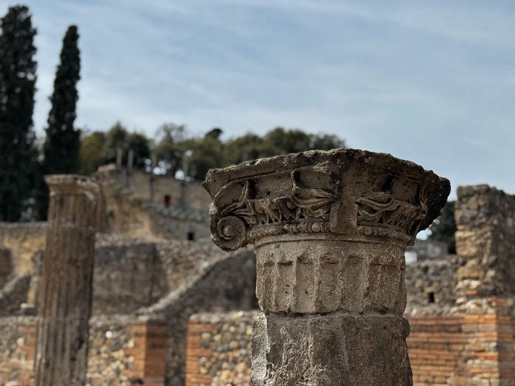 Ancient Roman ruins with a close-up of a decorative stone capital on a column, with other columns and ruins in the background. Shot in Pompeii italy