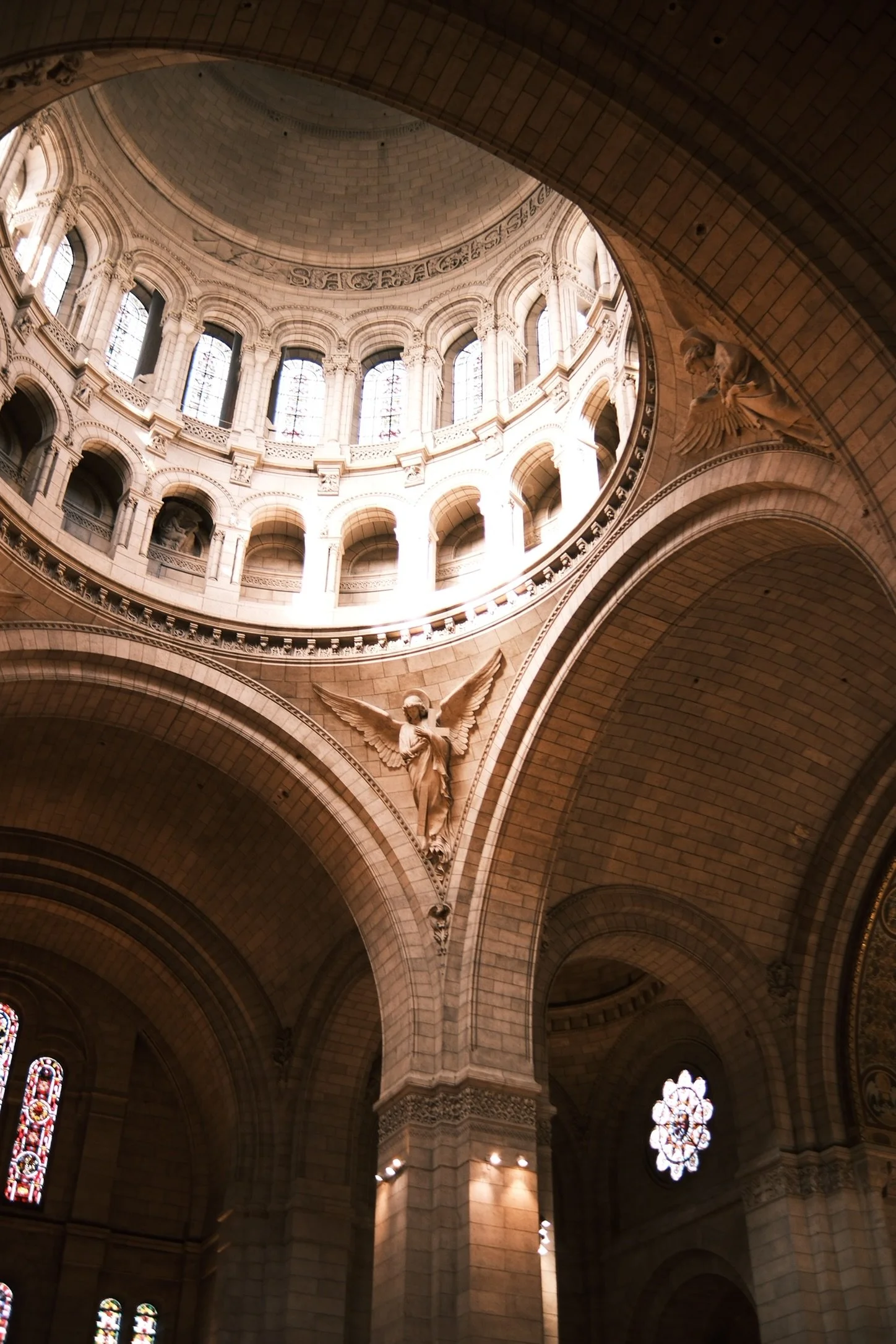 Interior view of theBasilica of Sacré-Cœur de Montmartre in Paris. Picture includes arches, stained glass windows, and a large dome with skylight at the top, featuring sculptures and architectural details.