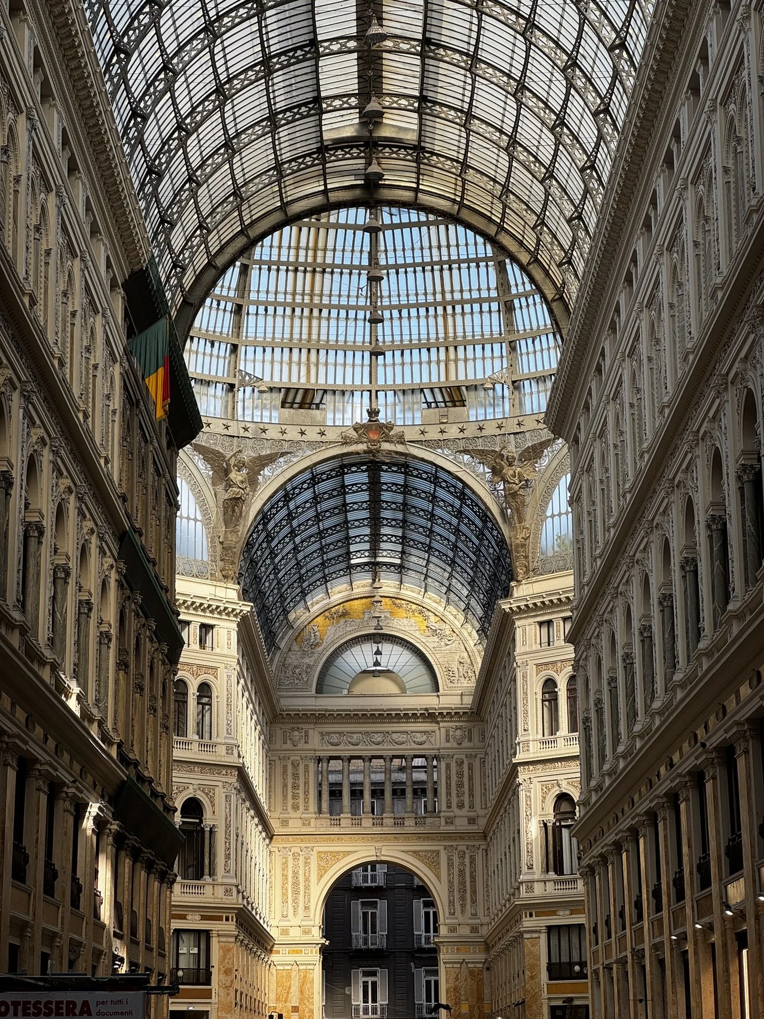 Interior of a historic shopping arcade with ornate architectural details, glass-domed ceilings, and decorative sculptures. Shot in Naples, Italy