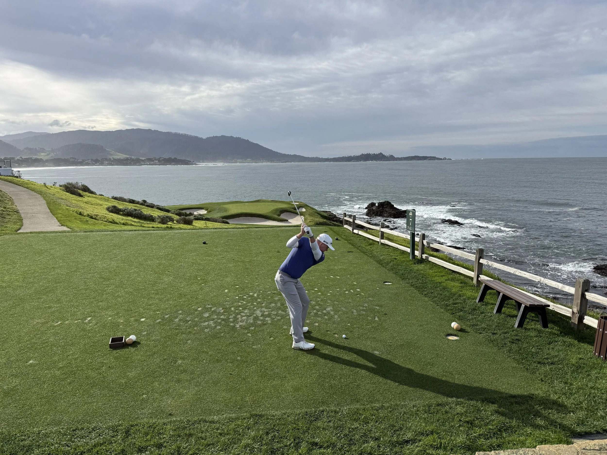 Golf course with a green and flag overlooking an ocean and distant land in the background.