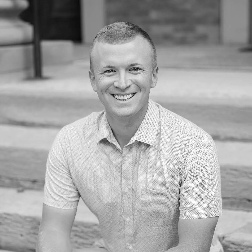 Taylor Suggs, smiling, wearing a collared shirt, sitting outdoors.