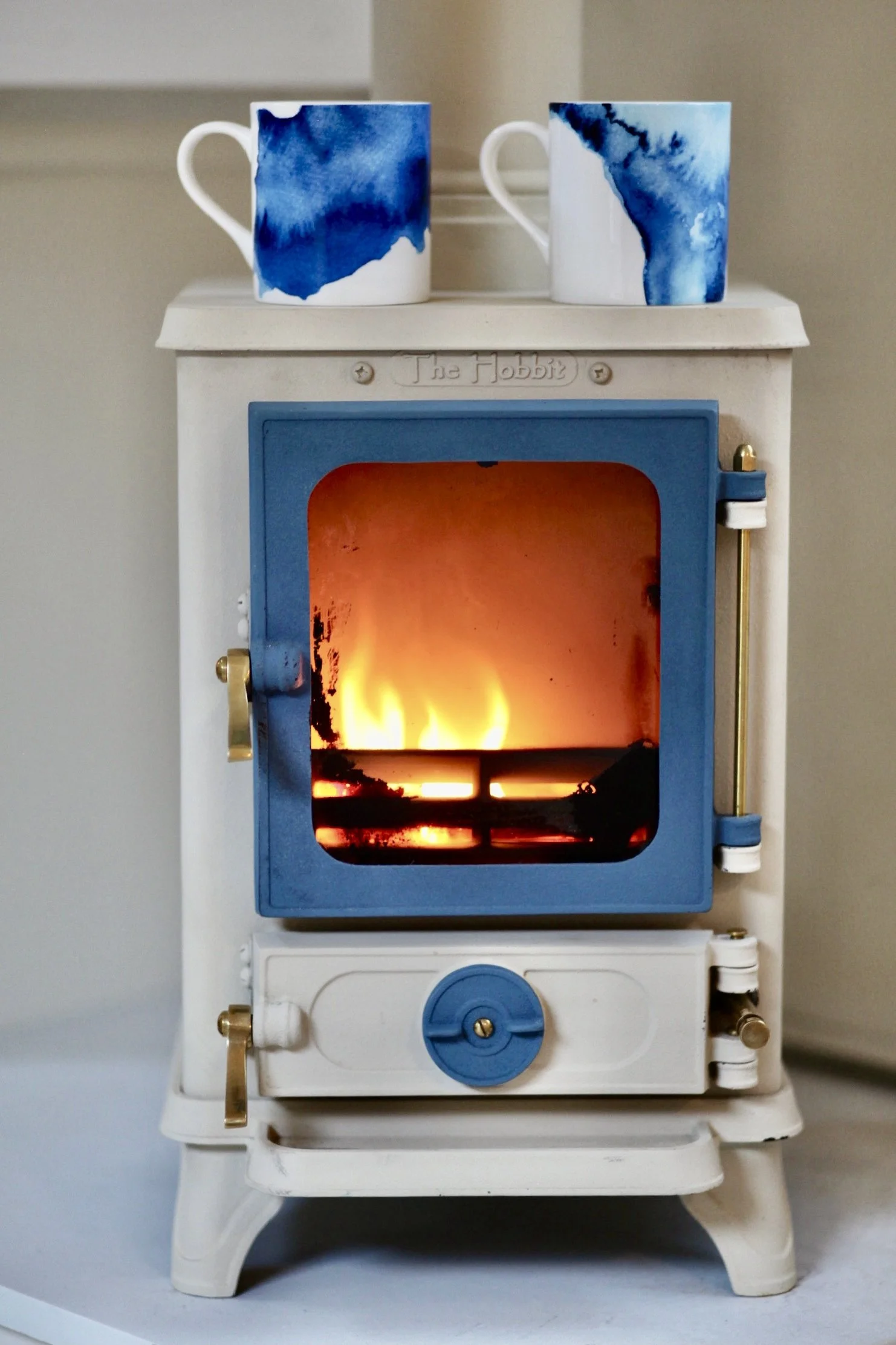 Miniature toy stove with a fire inside and two ceramic mugs with blue watercolor designs on top.