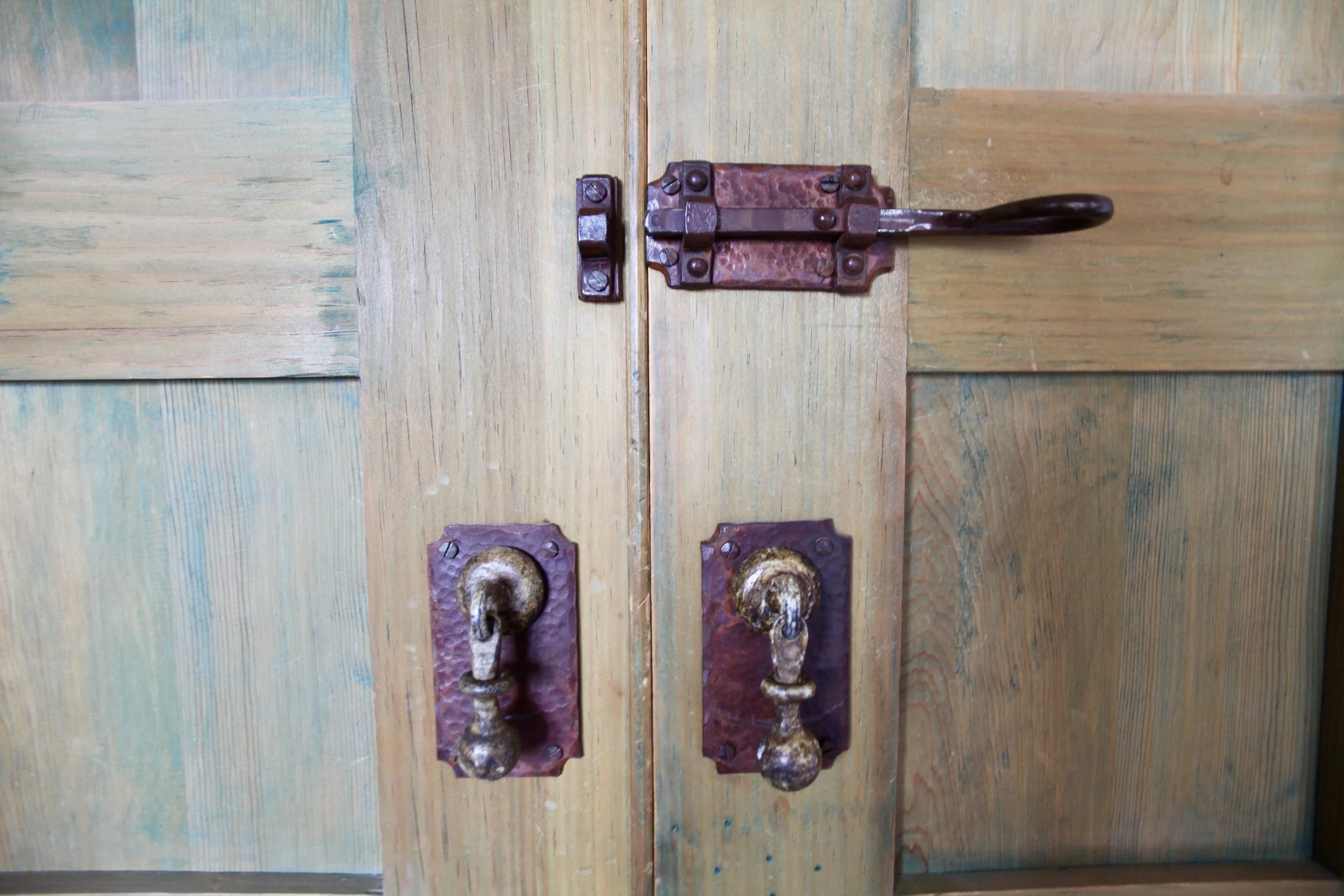 Close-up of a wooden door with two ornate brass door handles and an old-fashioned latch on the top.