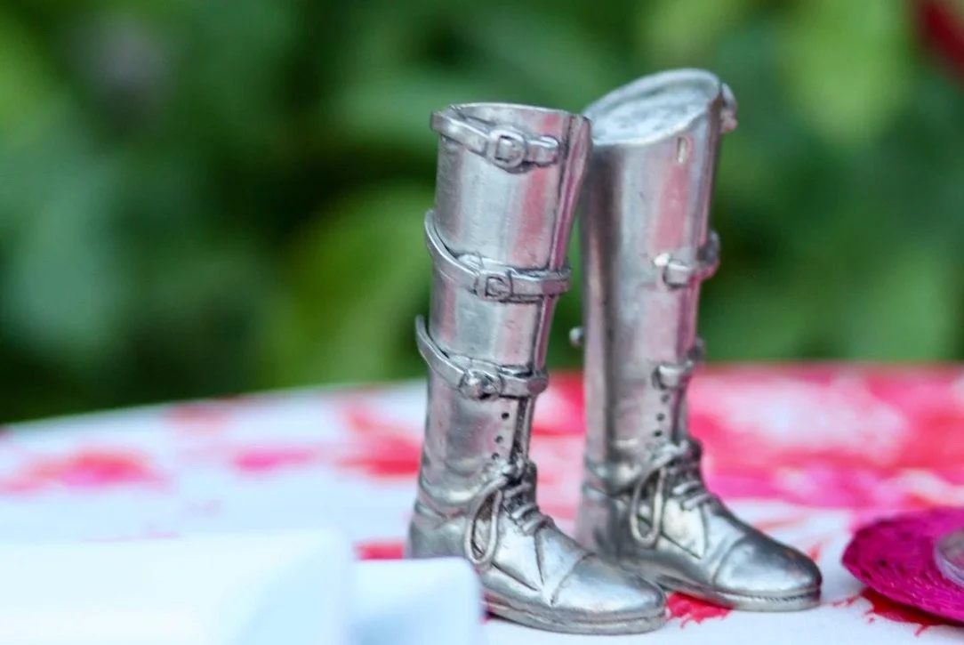 A pair of shiny silver metallic boots, resembling armor, resting on a cloth with a floral pattern.