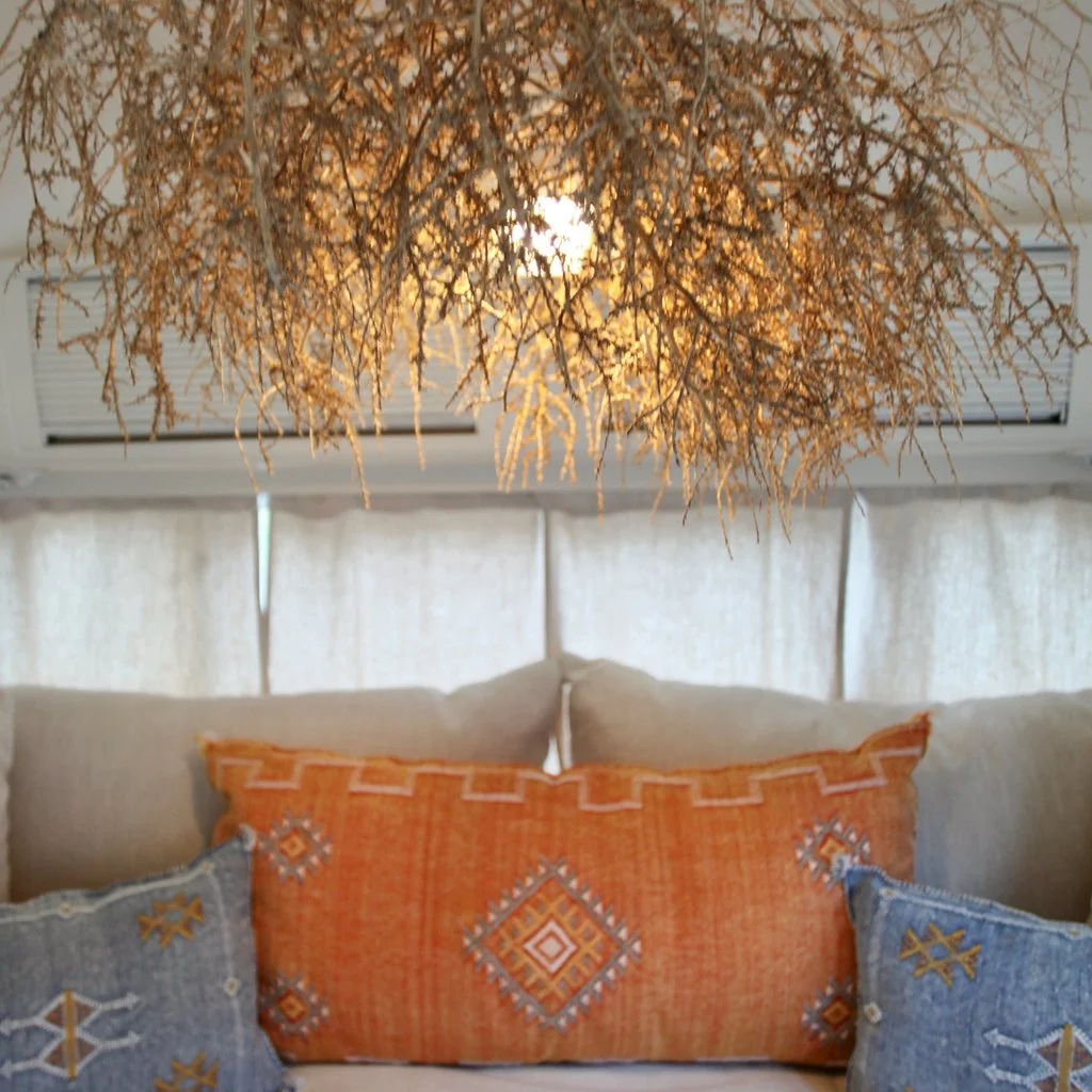 A close-up of a cozy seating area with colorful decorative pillows and a hanging light fixture made of twigs or branches.