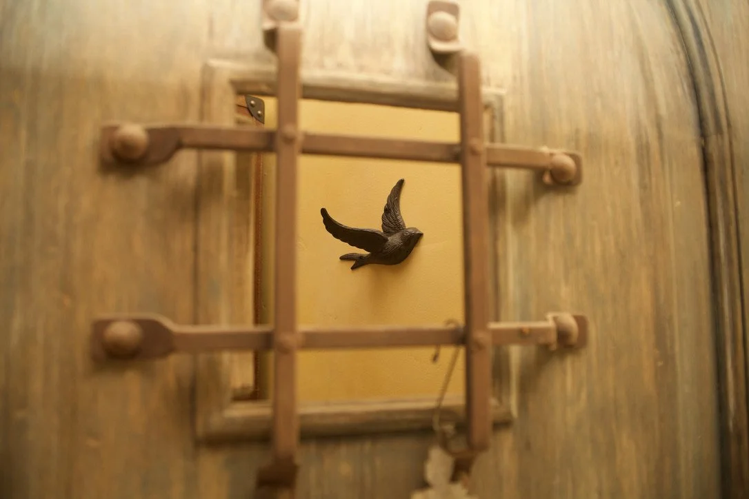 A small wooden framed mirror with a decorative flying bird sculpture mounted on a yellow wall reflected in it.