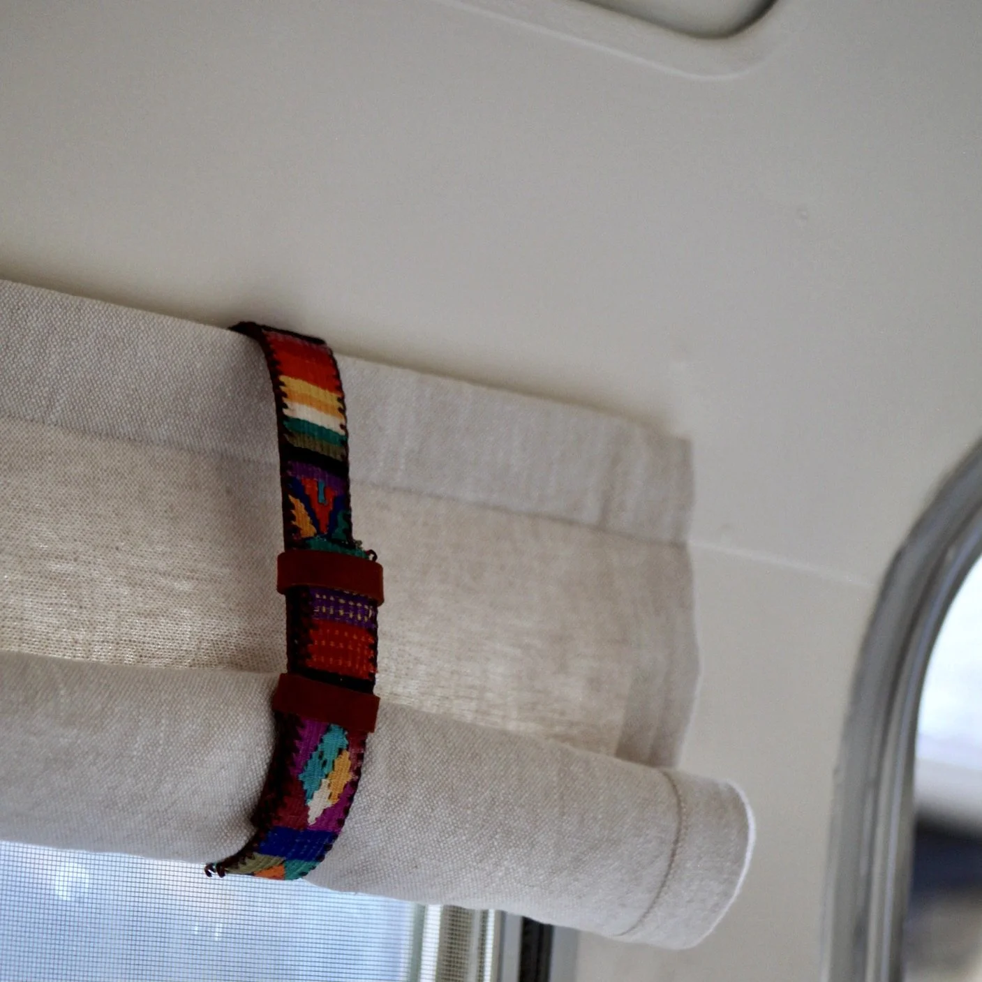 Colorful woven fabric strap attached to a beige curtain above a window.