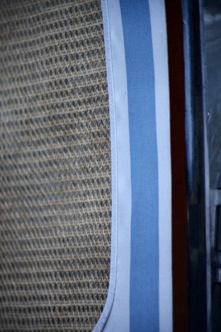 Close-up of a woven rattan surface, next to a blue and white striped fabric, with part of a dark brown wooden edge visible.