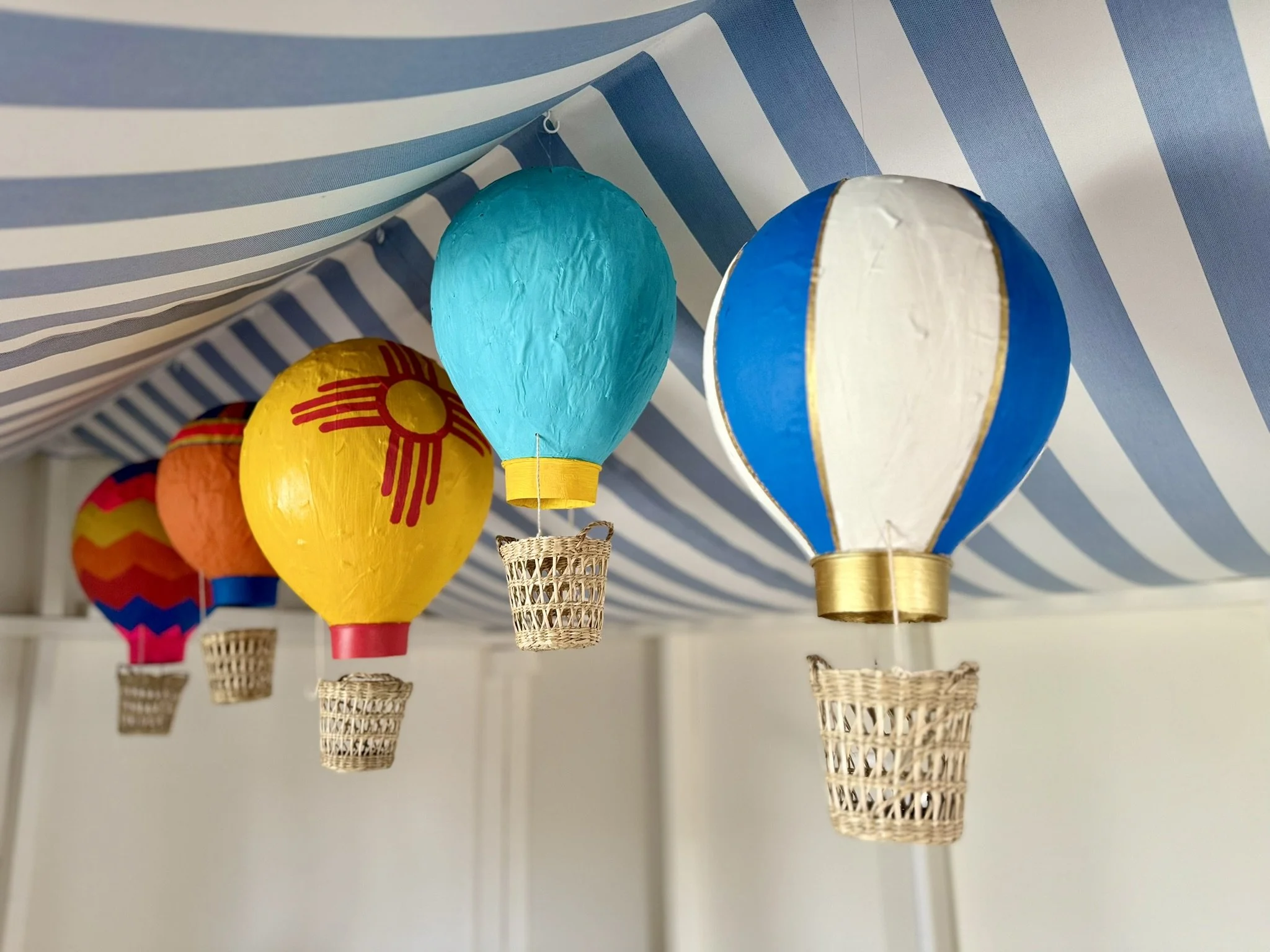 Colorful hot air balloon decorations hanging from a canopy with blue and white stripes.
