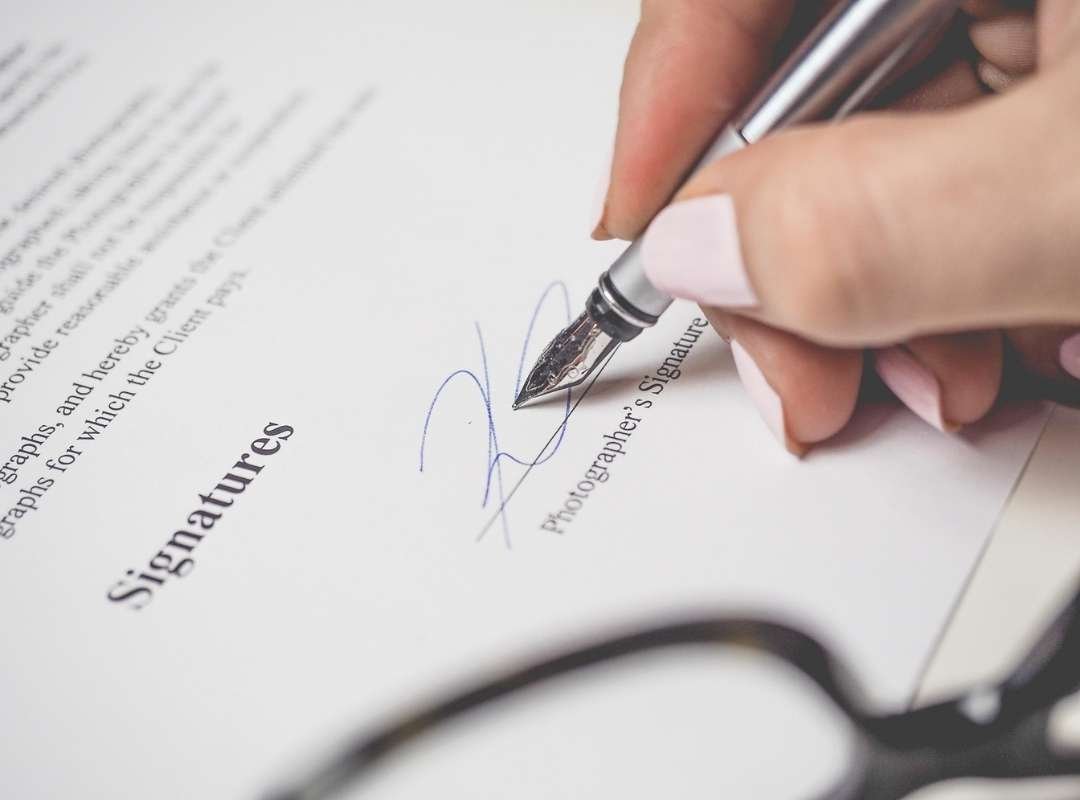 A person signing a document with a silver pen.