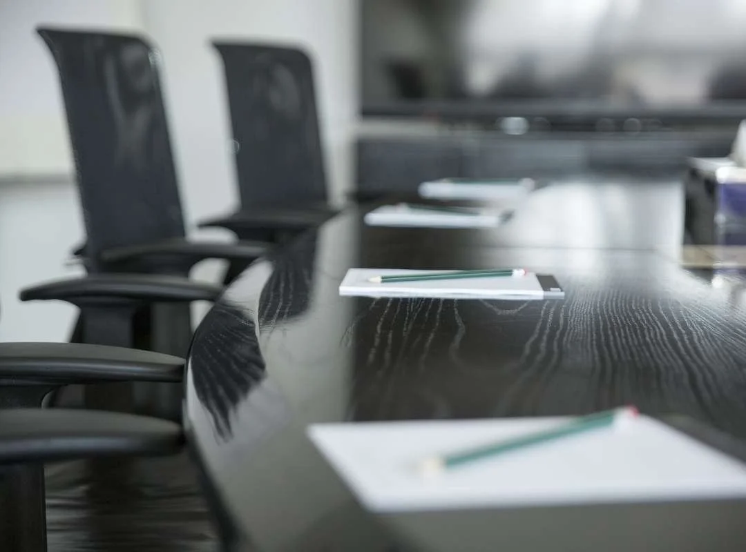 Empty conference room with a long black table, black office chairs, and notepads with pencils placed on the table.