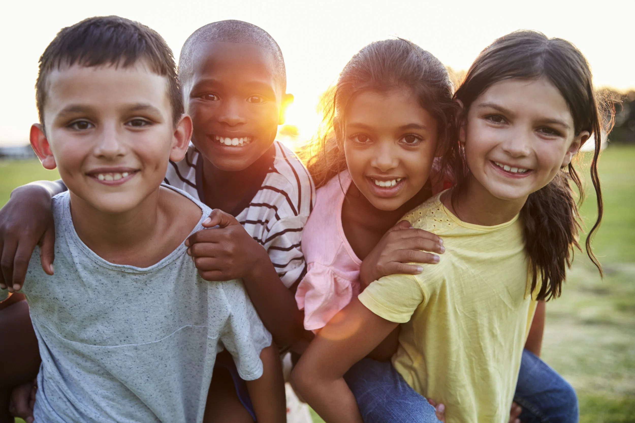 Group of four children smiling and posing outdoors at sunset.