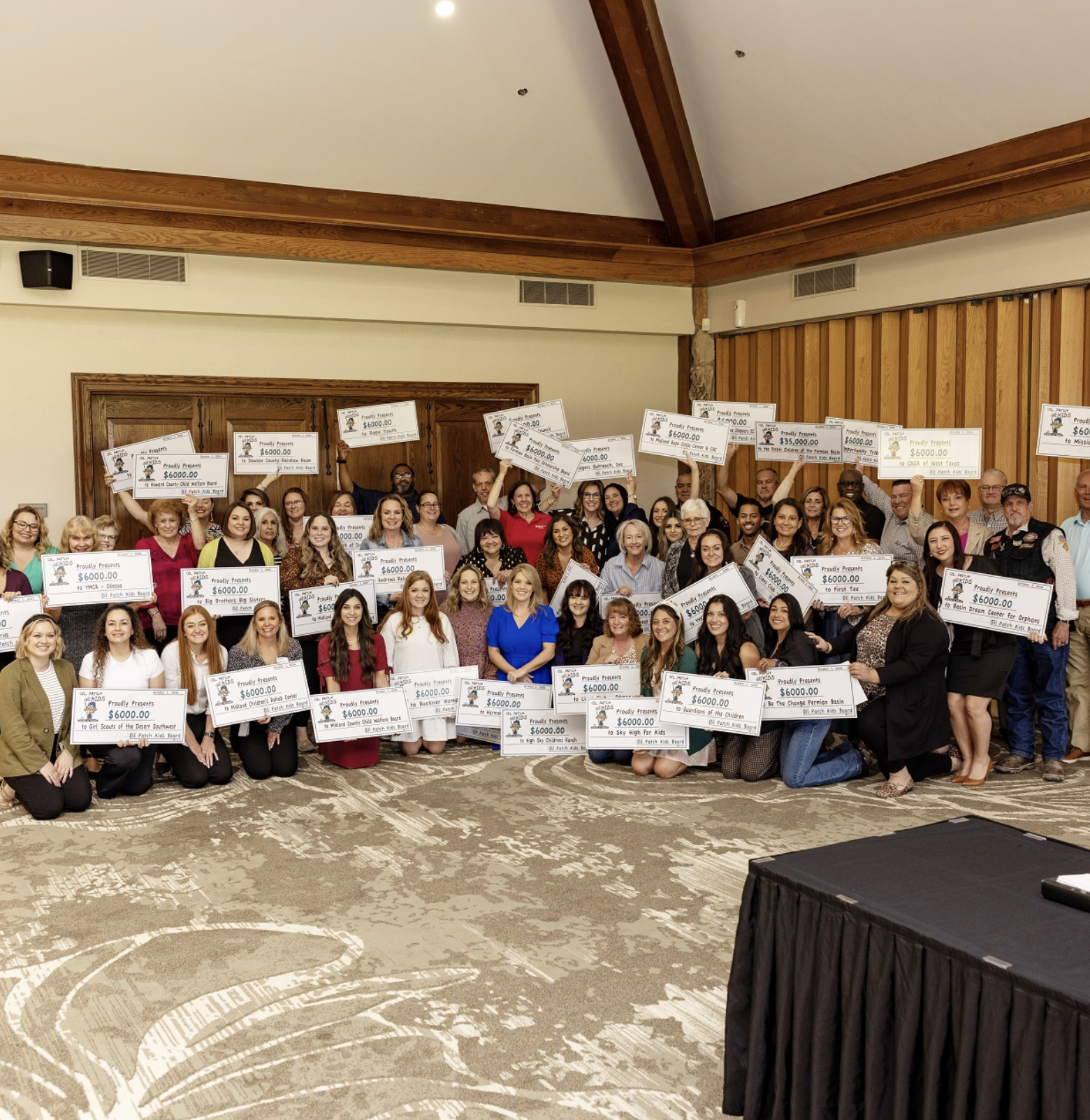 A large group of people in a banquet room holding oversized checks, celebrating a fundraising event.
