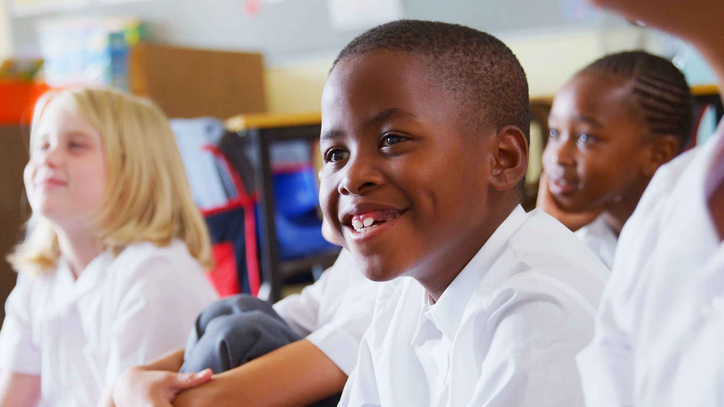 Young students sitting in a classroom, smiling and engaging during class.