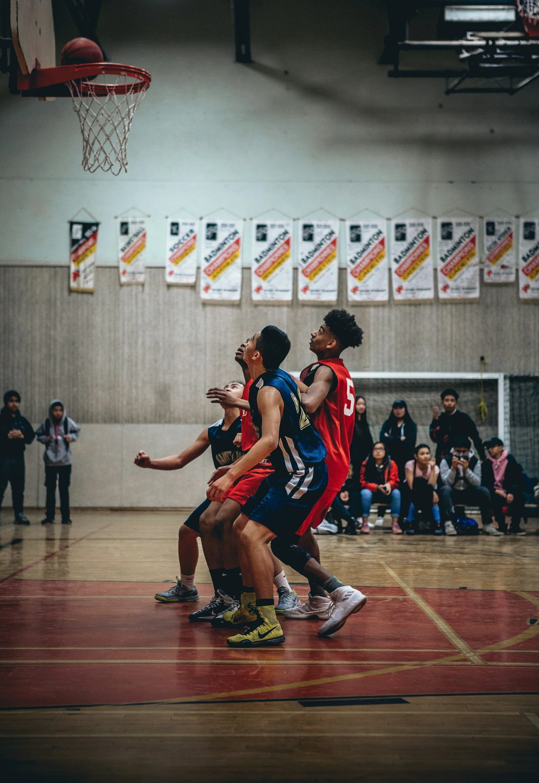Young boys playing basketball on an indoor court, with spectators seated in the background.