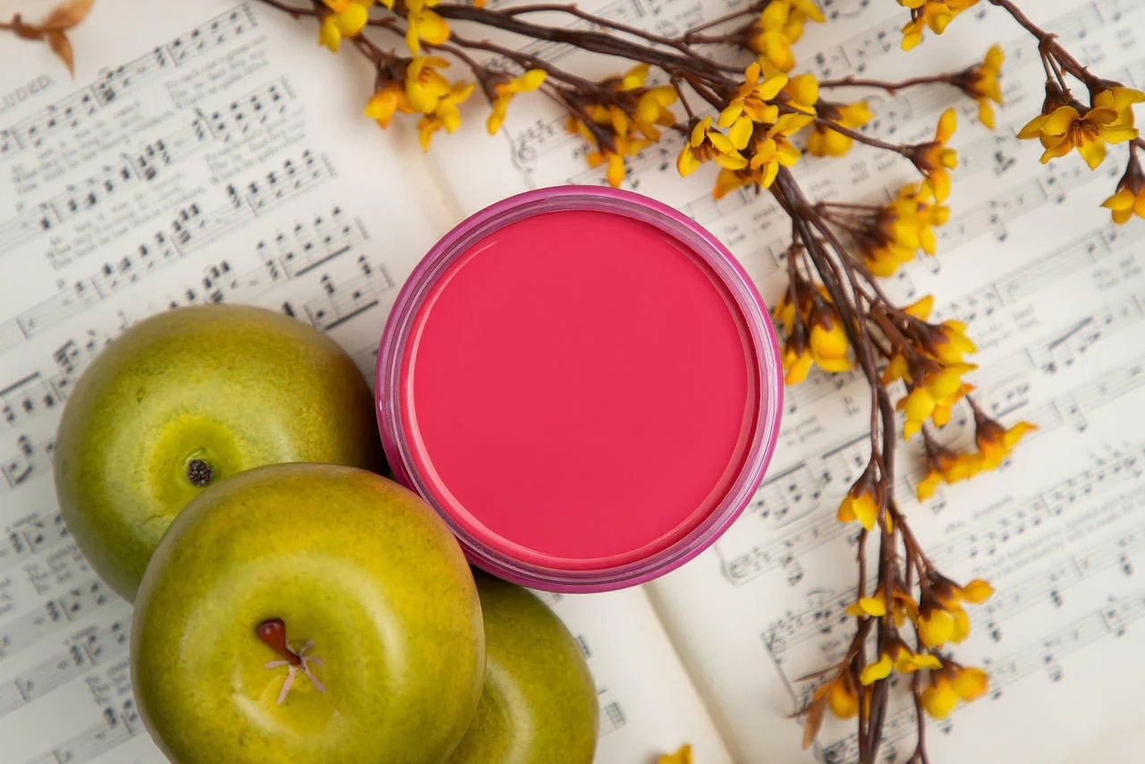 Green apples, a pink candle, and yellow flowers on sheet music.