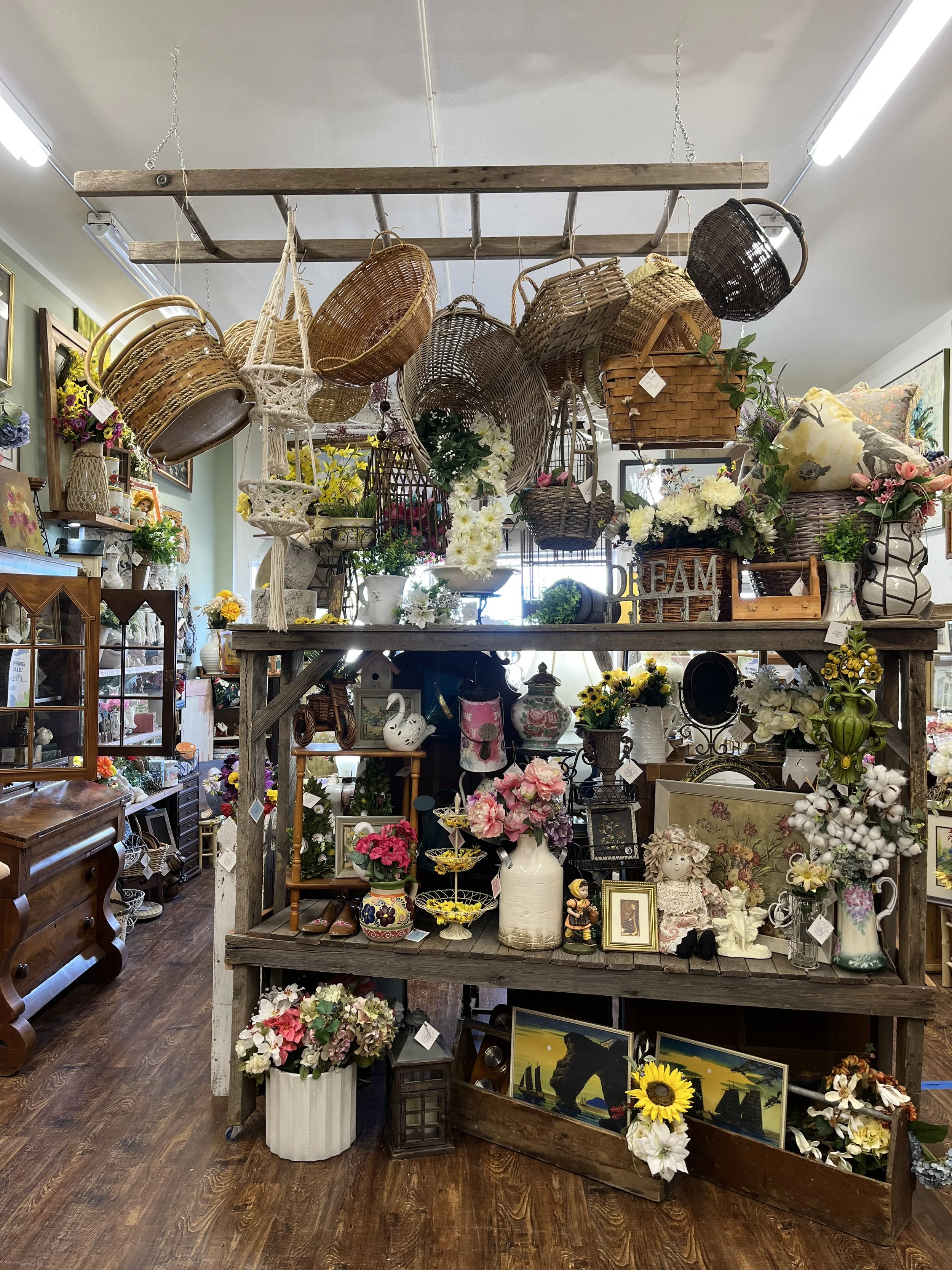 Interior of a thrift or antique store with various baskets, vases, and floral arrangements on shelves and tables.