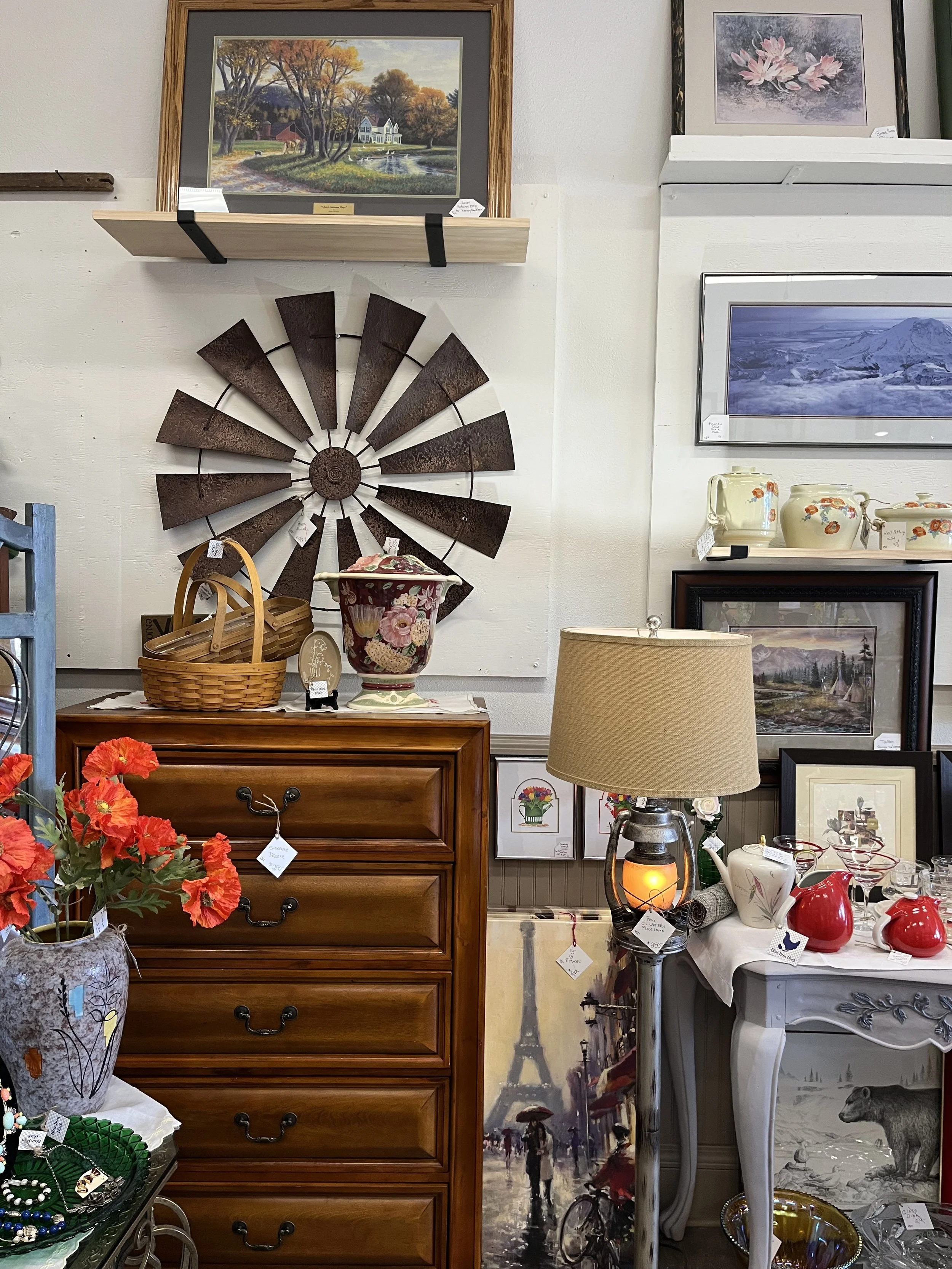Wall decor and furniture in an antique shop displaying artwork, lamps, ceramics, jewelry, and decorative items.