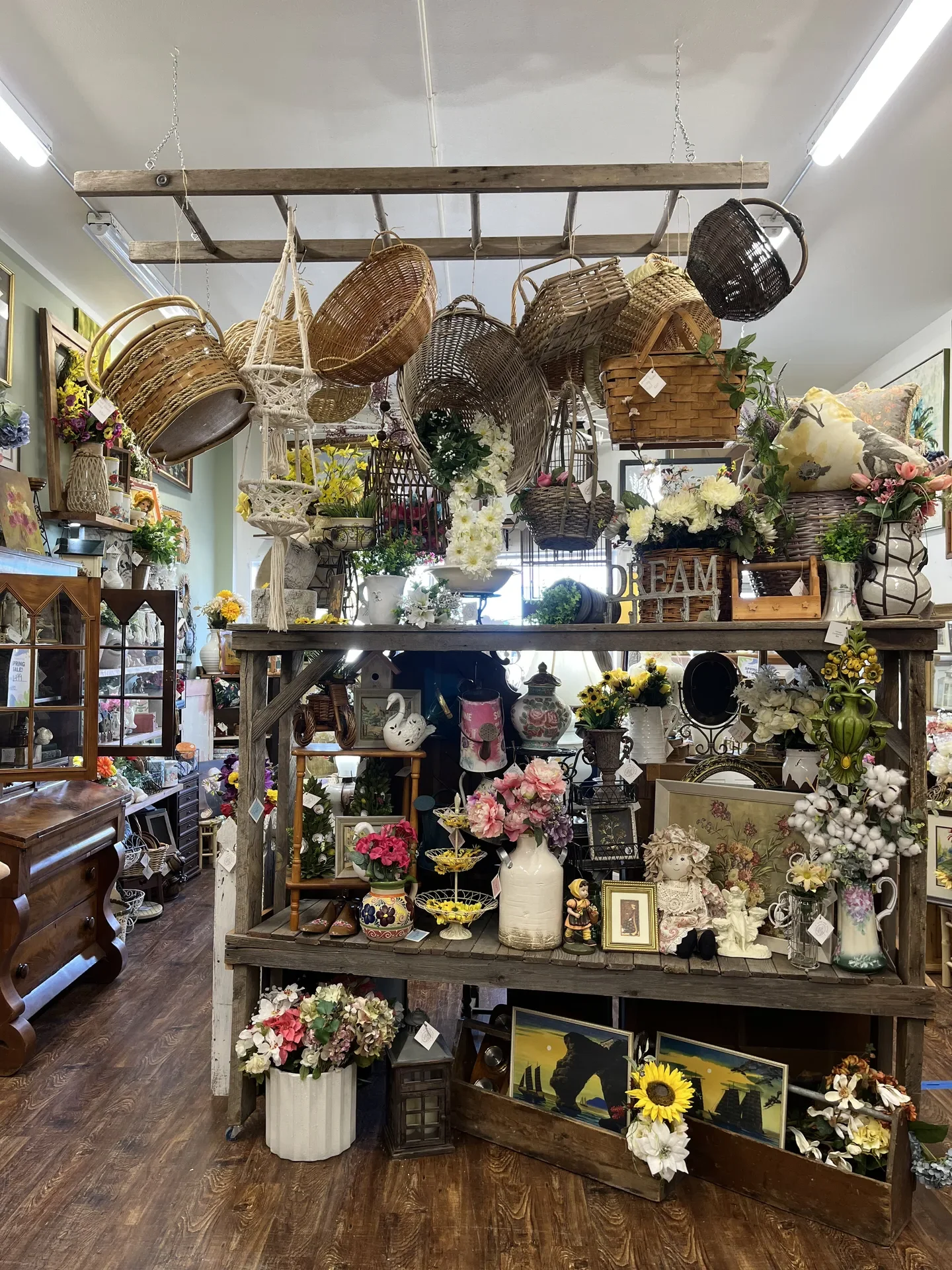 Interior of a thrift or antique store with various baskets, vases, and floral arrangements on shelves and tables.