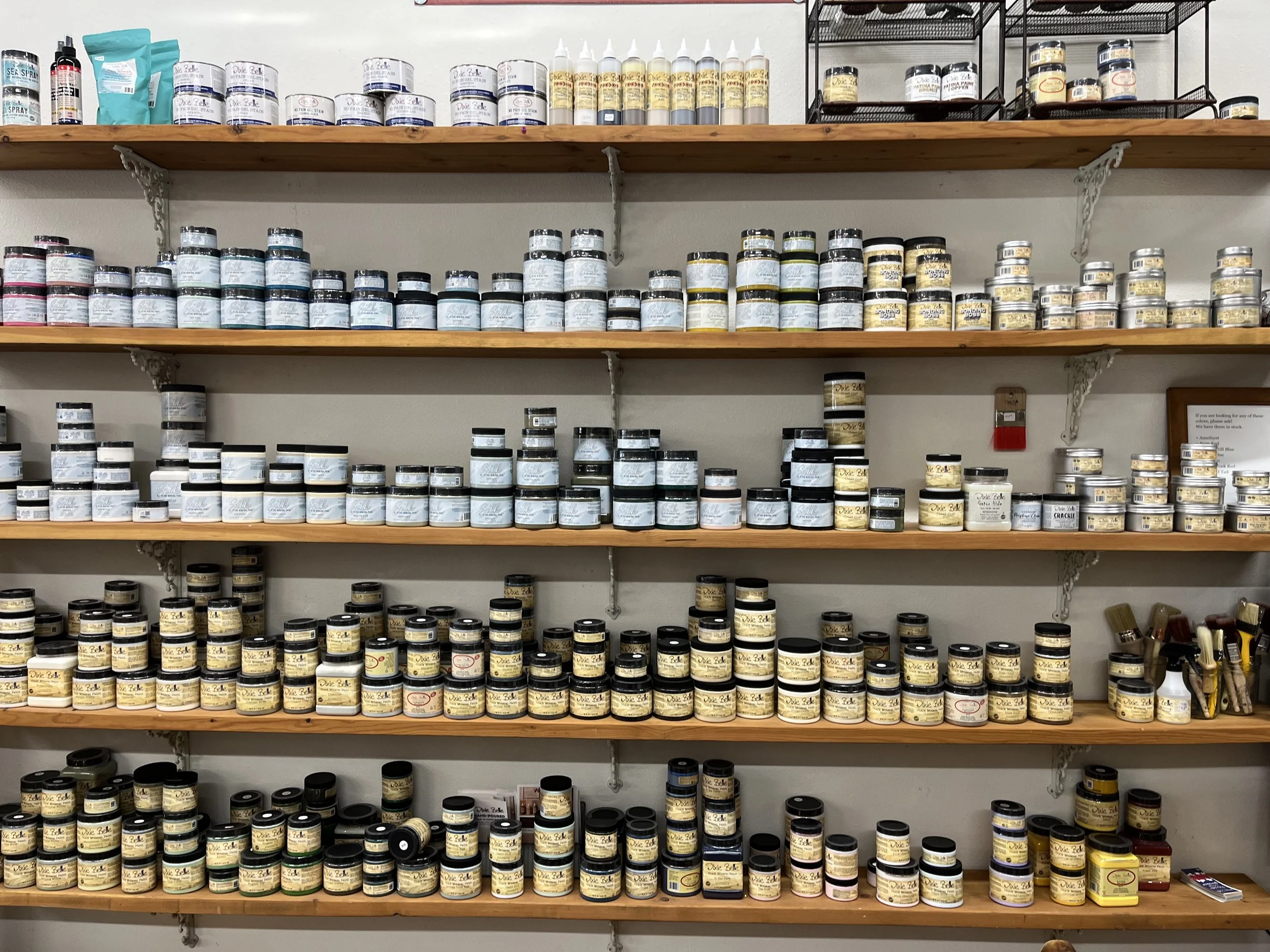 Wooden shelves holding various jars of Dixie Belle chalk paint in different colors and sizes in a store.