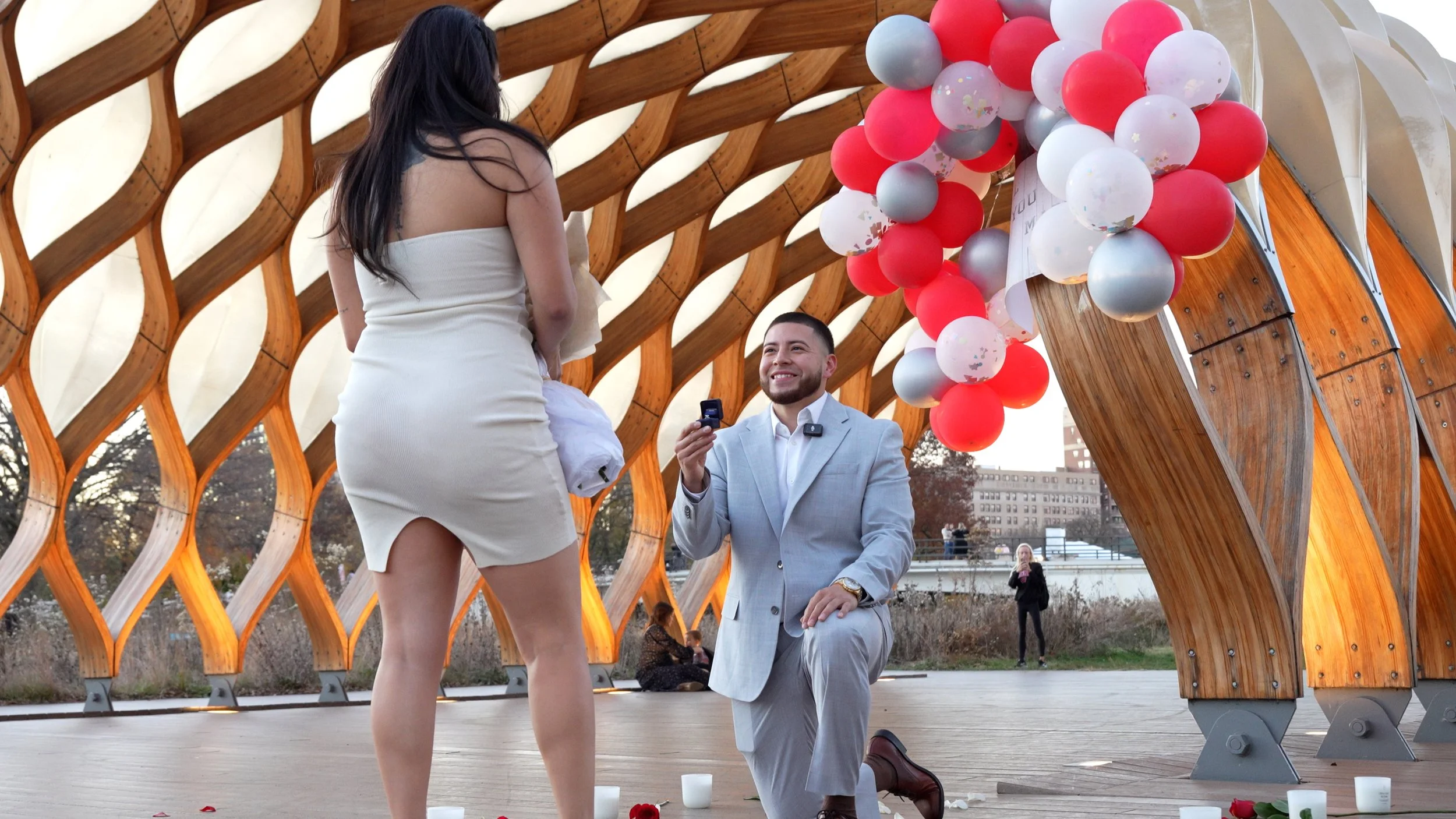 A man proposing marriage to a woman during a romantic outdoor proposal event with balloons and candles.