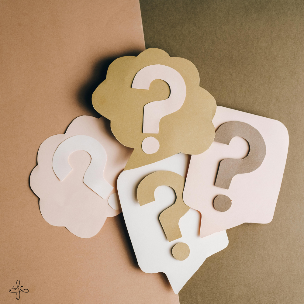 Diversi cartoncini a forma di nuvole con dei punti interrogativi in fila su uno sfondo composto da due colori, crema e beige.