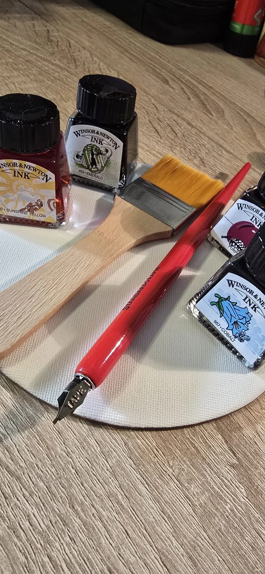 Set di inchiostri per tatuaggi con colori come giallo, nero, blu e viola, un pennello grande, una penna per tatuaggi rossa, e un sottofondo di tavola di legno.