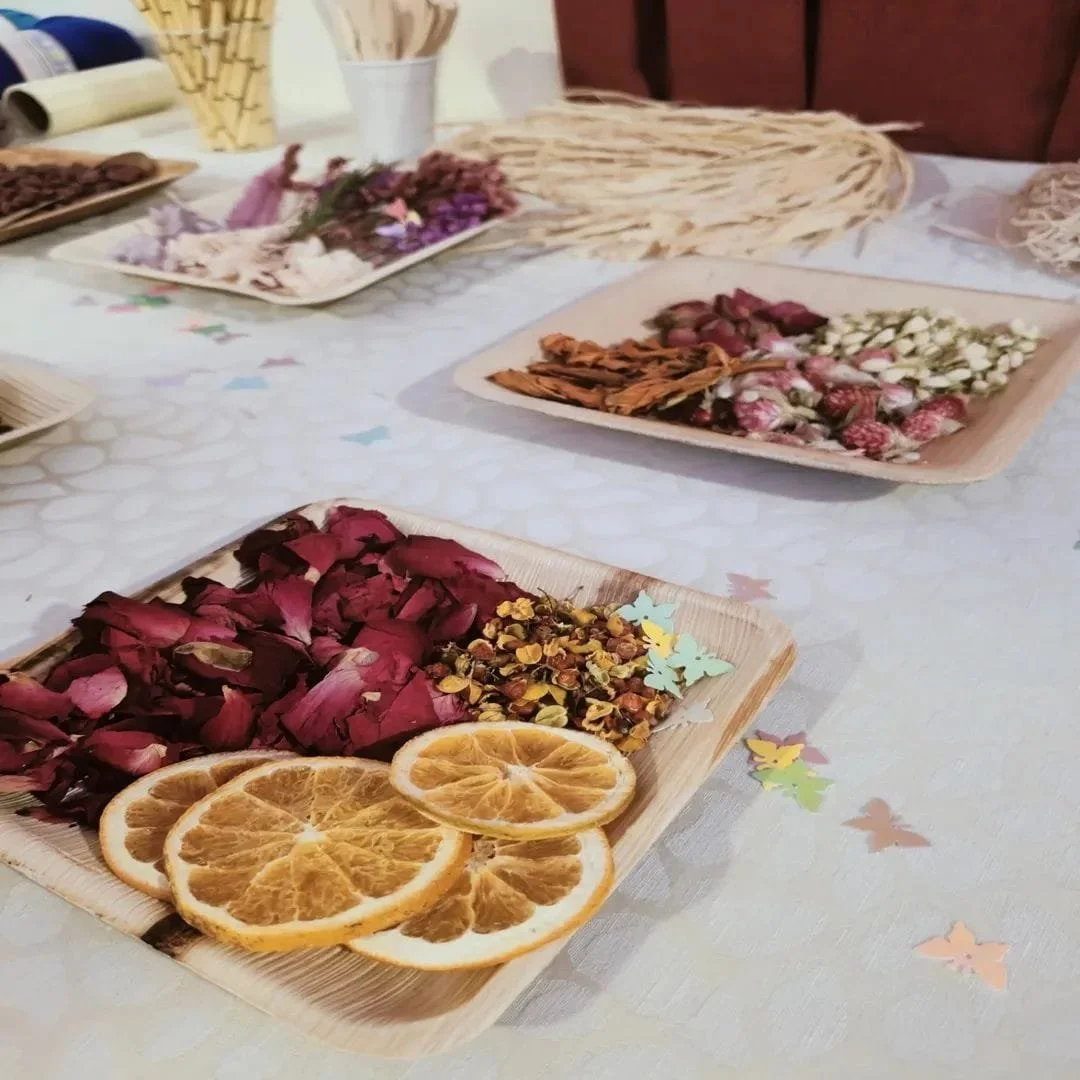 Piatti di fiori secchi, fette di arancia e petali di rosa su un tavolo decorato con farfalle di carta.