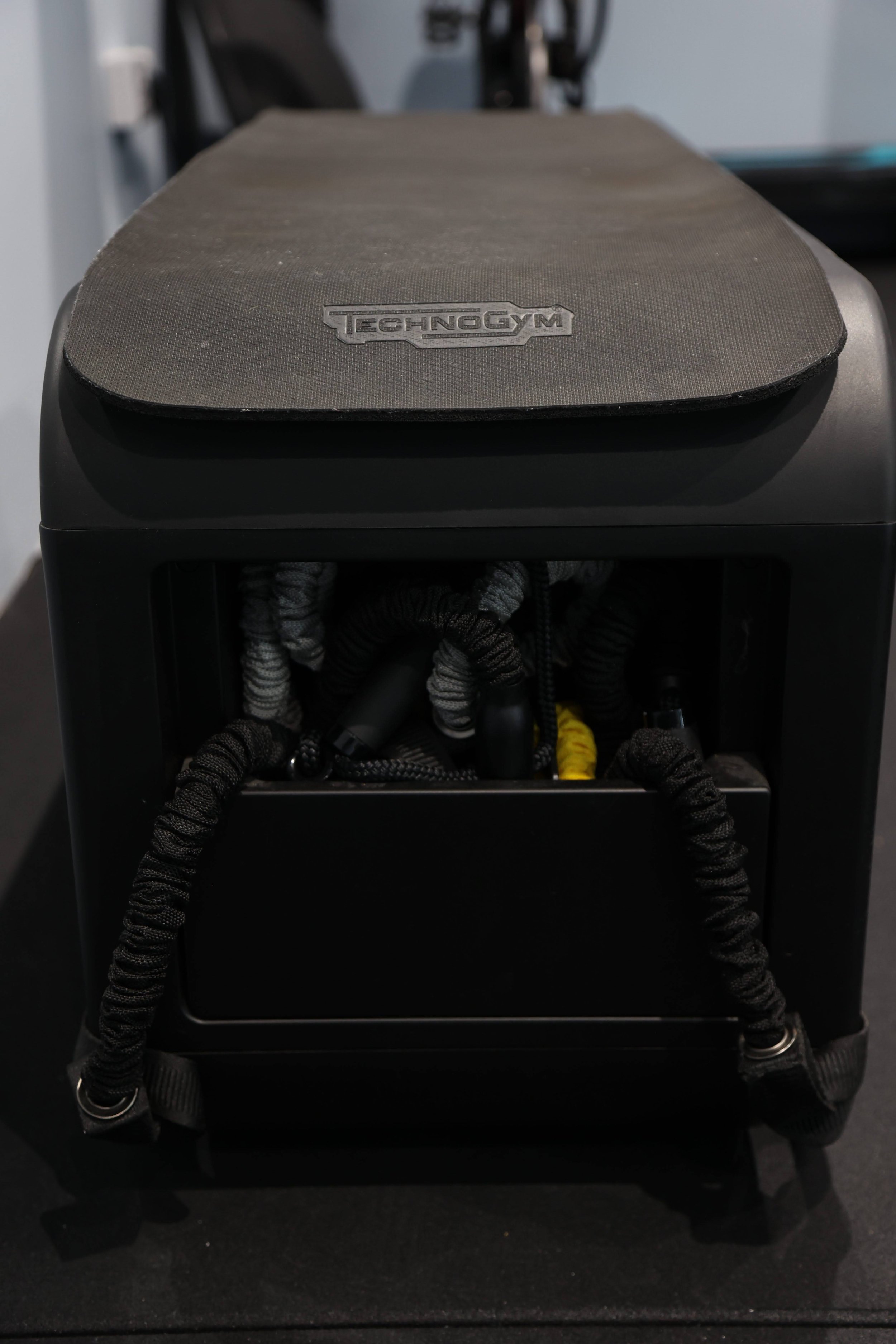 A black and gray TechnoGym box with tangled resistance bands hanging from it.