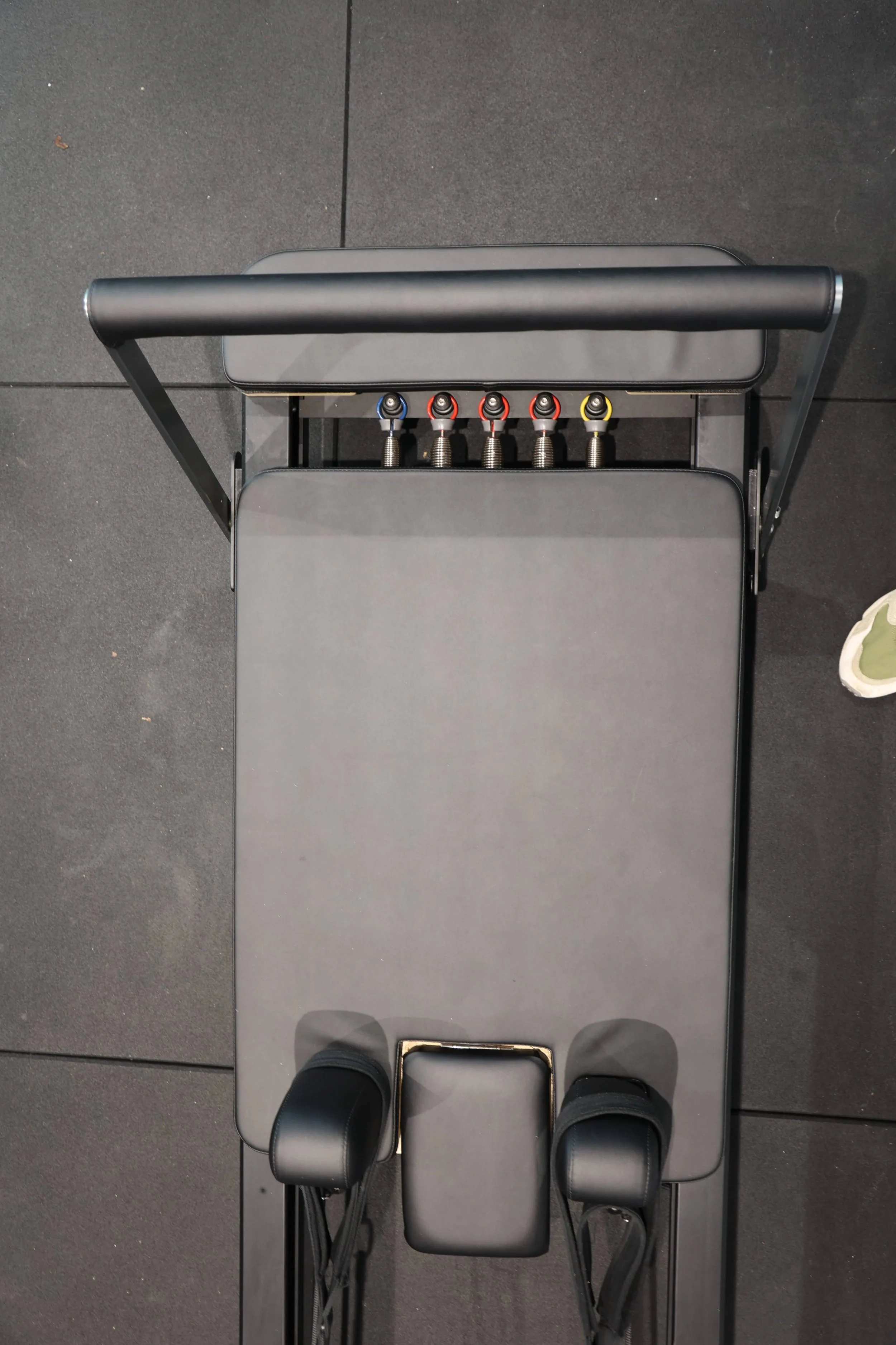 Overhead view of a person standing on a black treadmill with a black cushioned surface in a gym, shoes visible at the bottom of the frame.