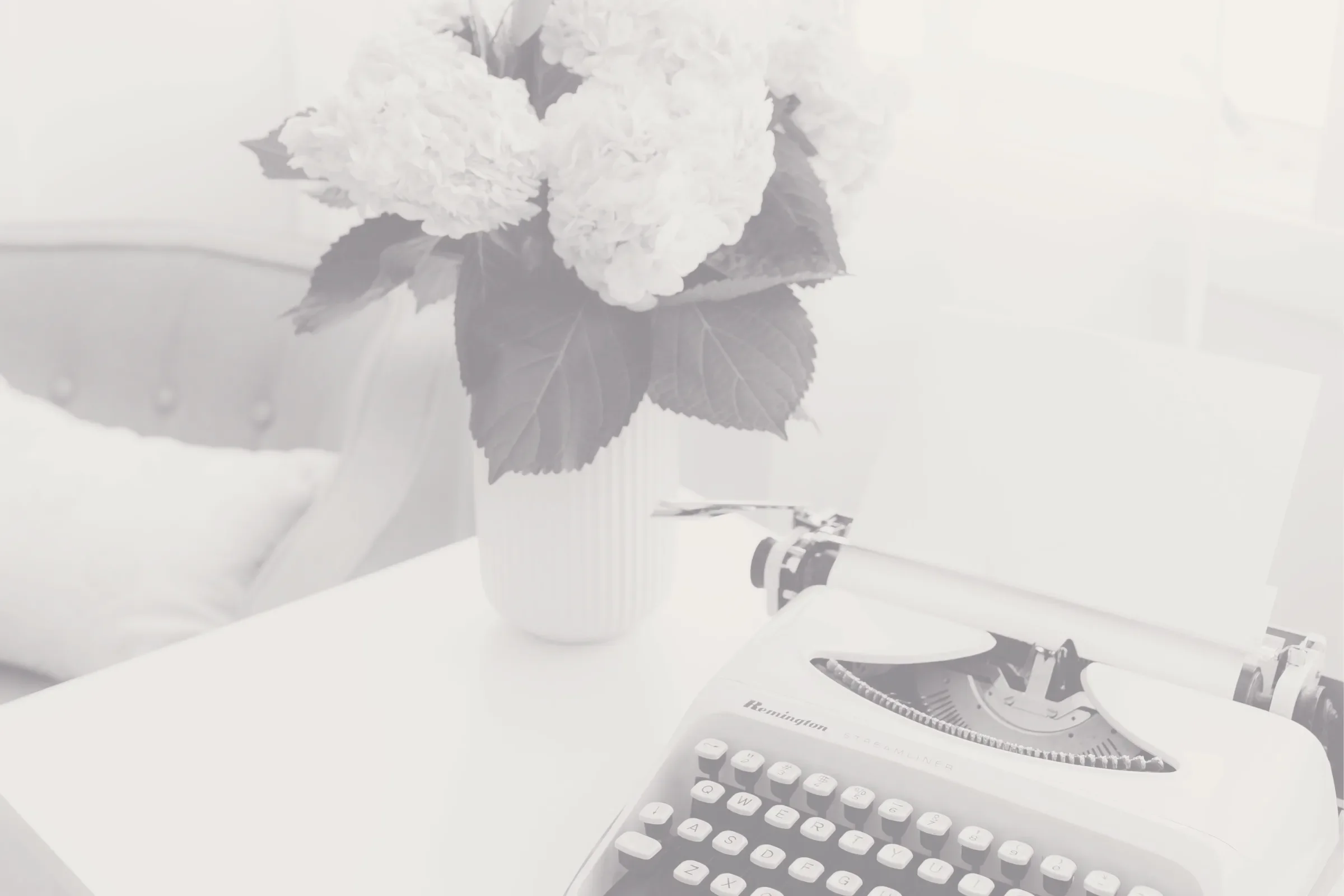 A desk with a potted hydrangea plant, a keyboard, and a vintage Remington typewriter on a white surface.
