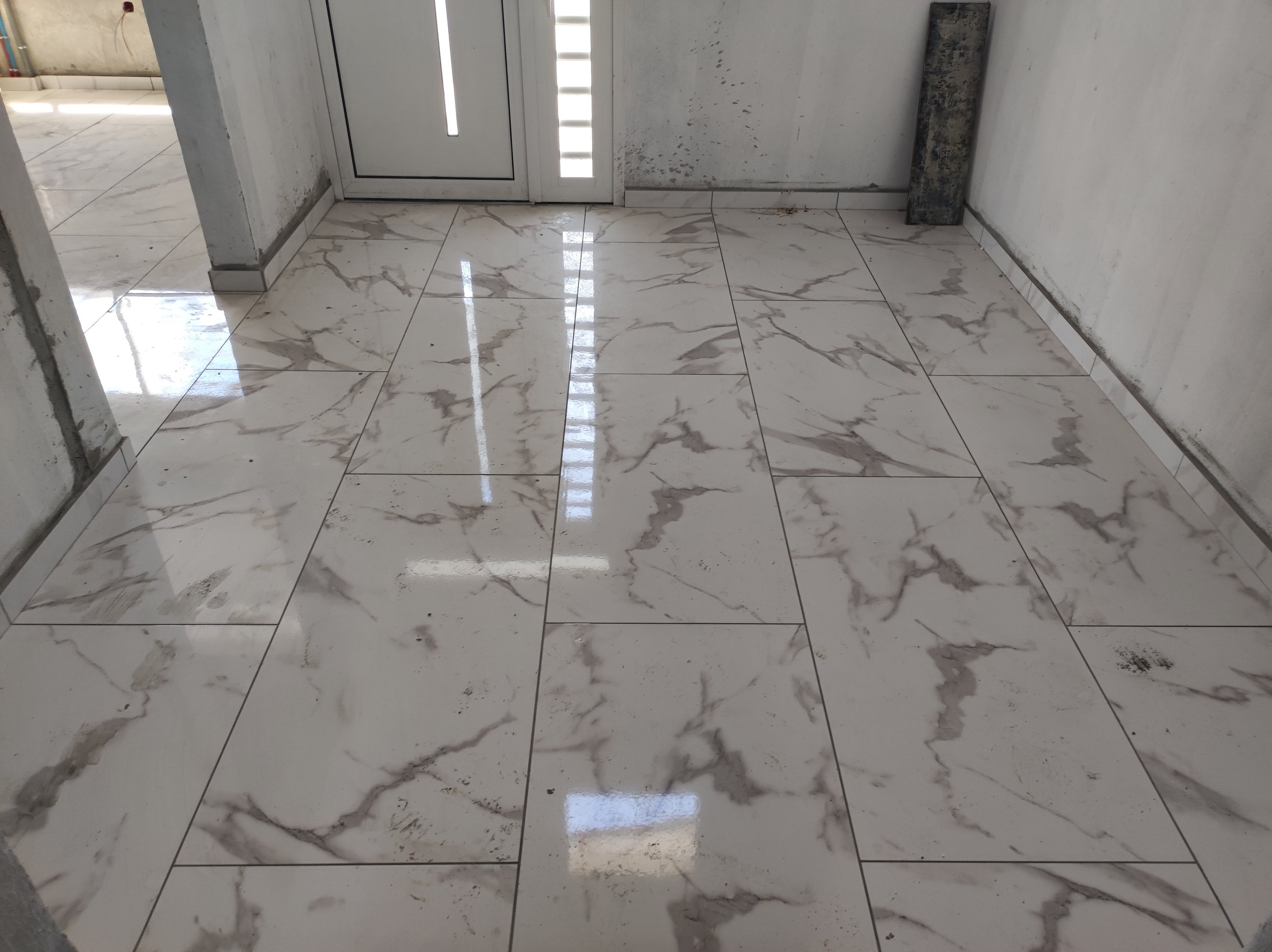 Sol en marbre brillant avec des veines brunes, dans une pièce en construction ou rénovée, avec murs en béton et une porte en métal