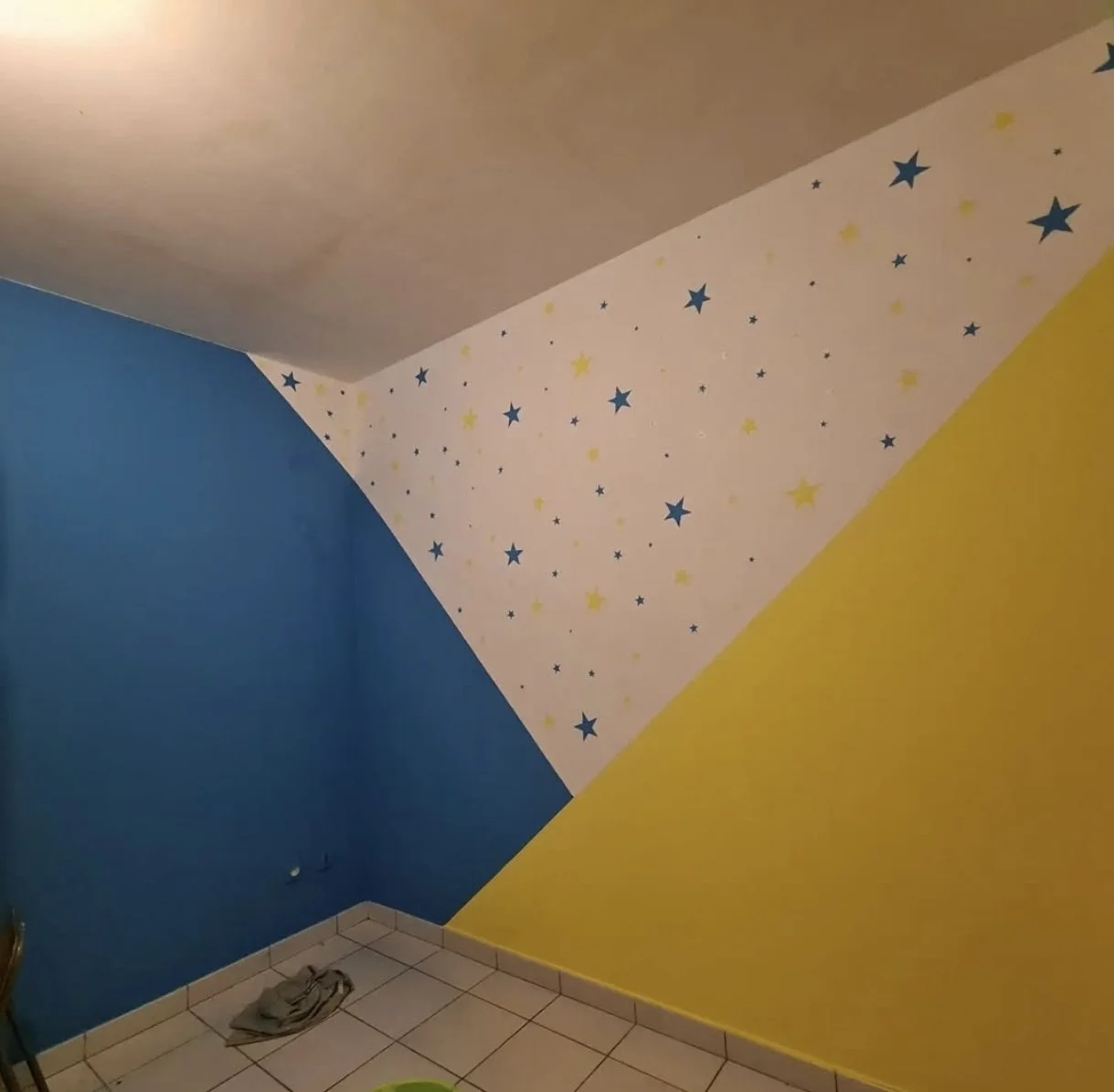 Mur avec peinture de couleur bleue et jaune, et une section de plafond avec motifs d'étoiles bleues et jaunes sur fond blanc.