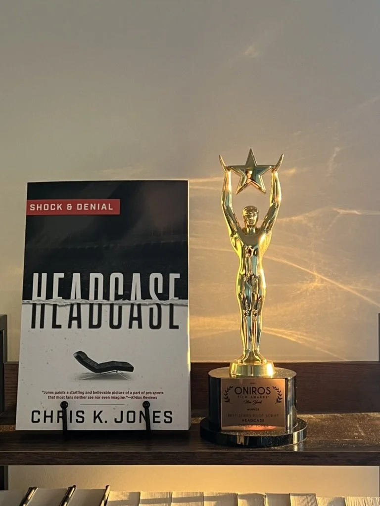 A trophy with a gold human figure holding a star, and a book titled 'Headcase' by Chris K. Jones next to it on a shelf.