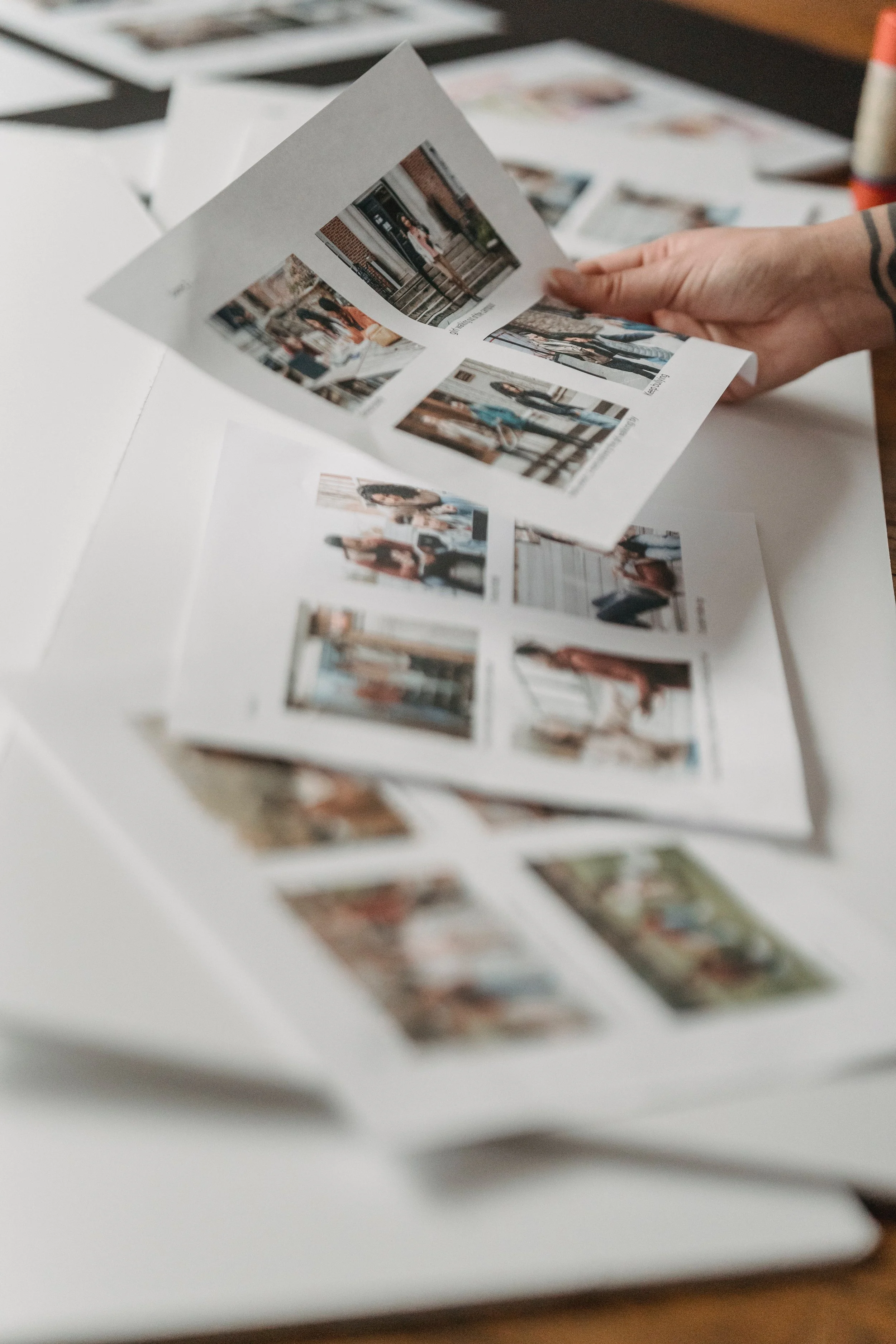 Person flipping through printed photo contact sheet with multiple small photos of people and locations.
