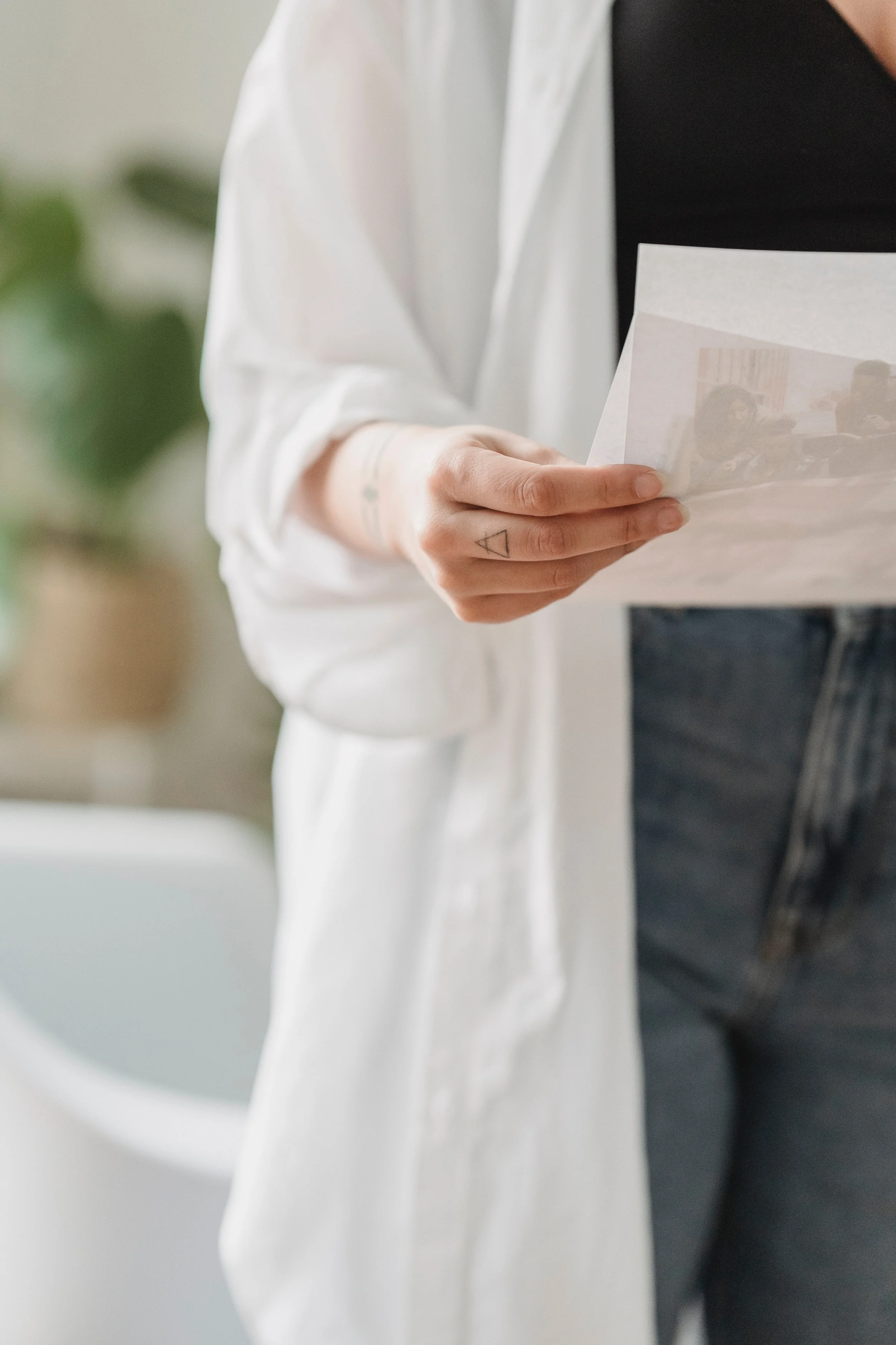 Person holding a paper in a casual setting, wearing a white open shirt over a black top and blue jeans.