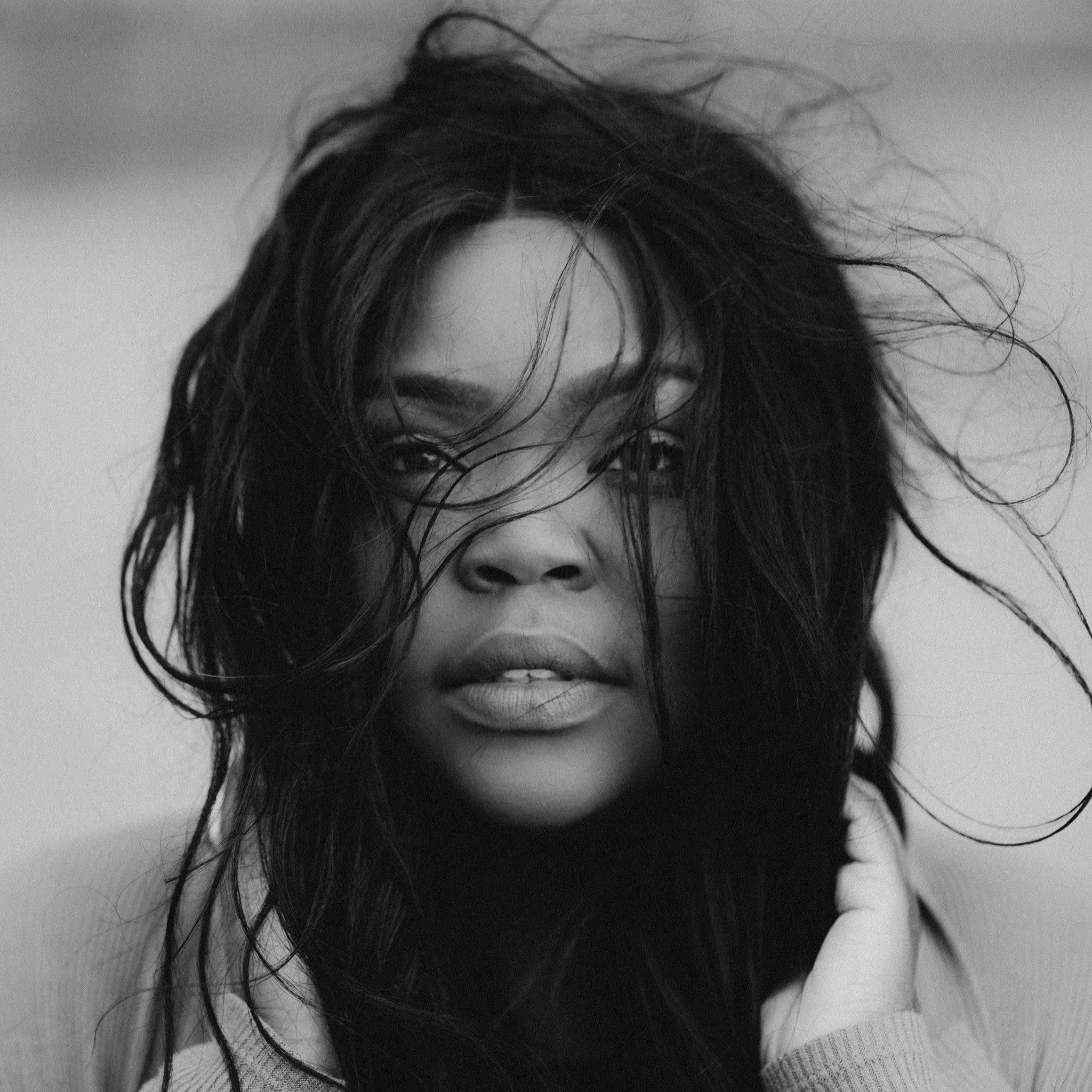 Black and white close-up portrait of a woman with messy hair partially covering her face, looking directly at the camera.
