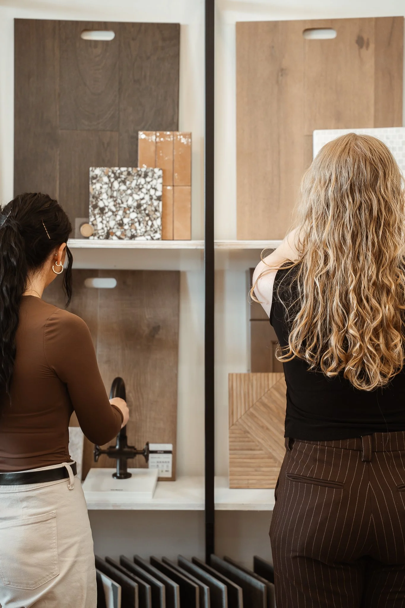 Two women shopping for home decor, viewing samples of tiles, wood, and other materials in a showroom.