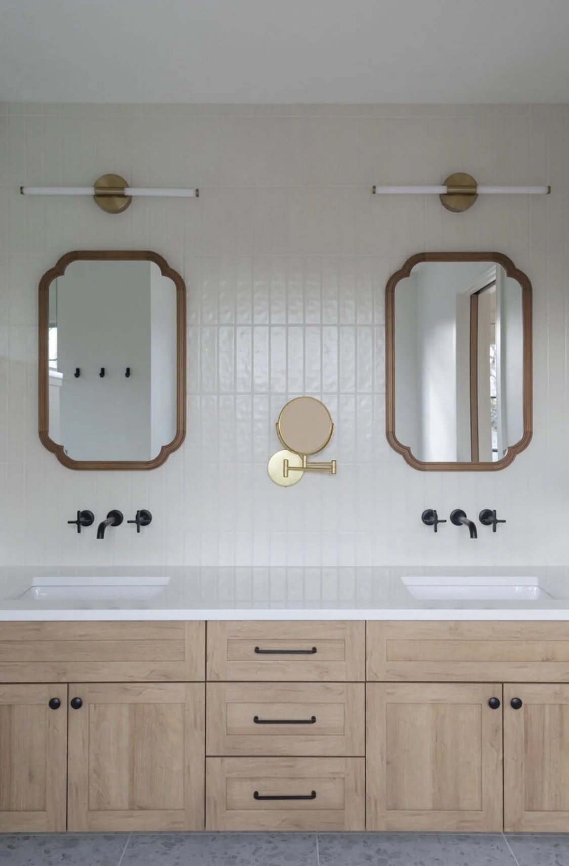 Double vanity bathroom with two oval mirrors, black faucet fixtures, and a light wood cabinet with black handles.