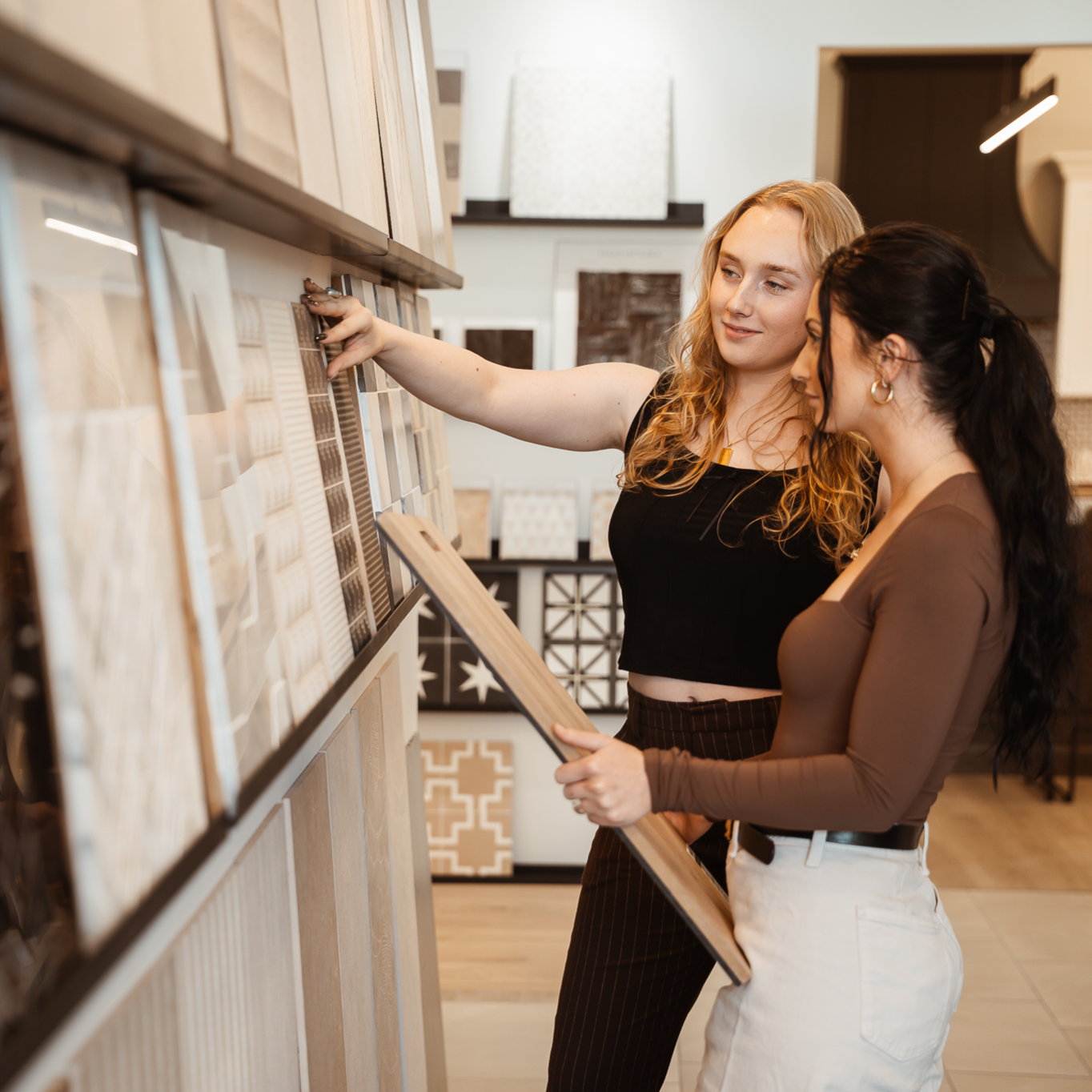 Two women shopping for home decor, looking at samples of tiles or wall panels in a store.