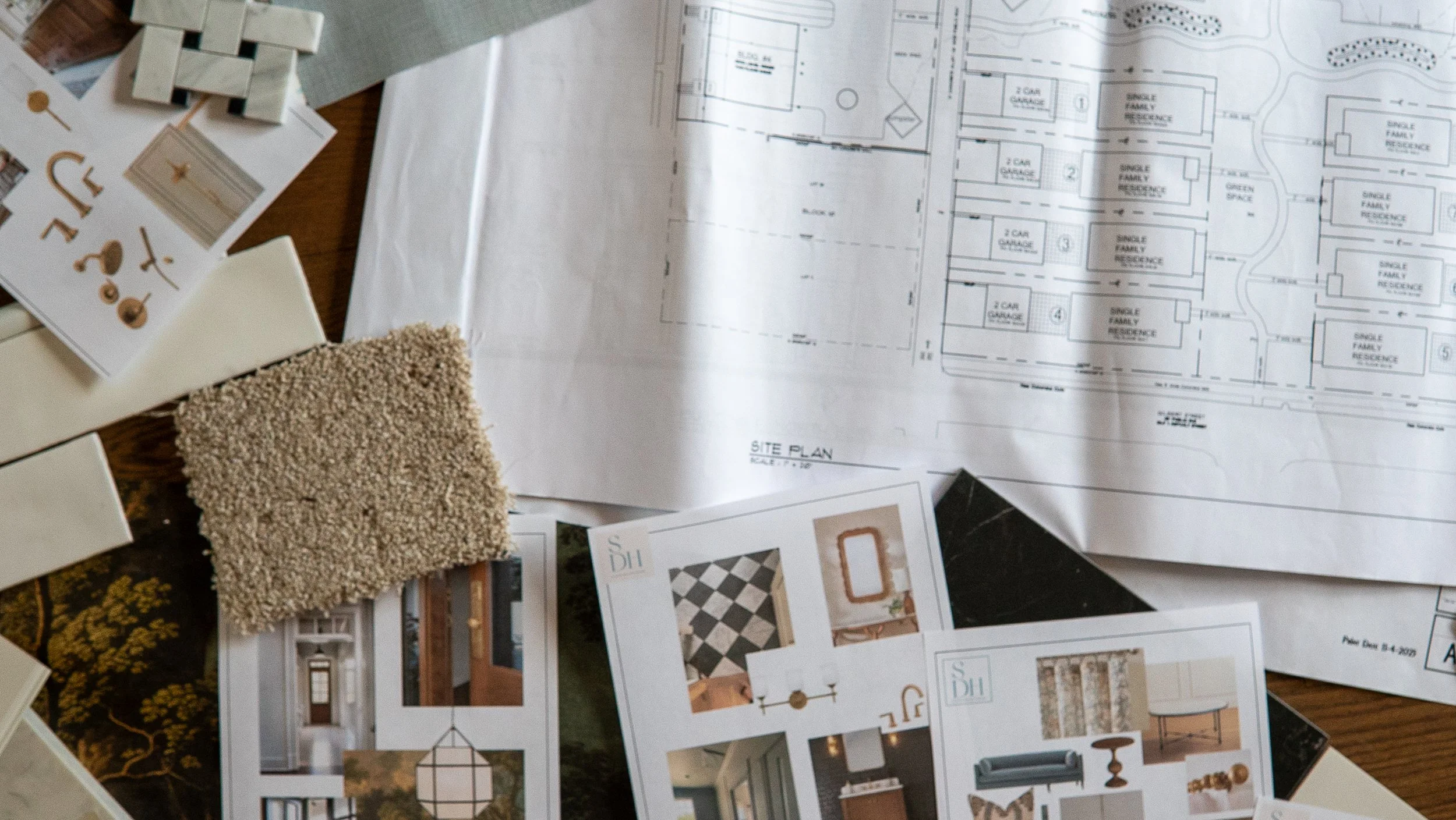 Architectural blueprints, interior design samples, and fabric swatches spread out on a wooden table.