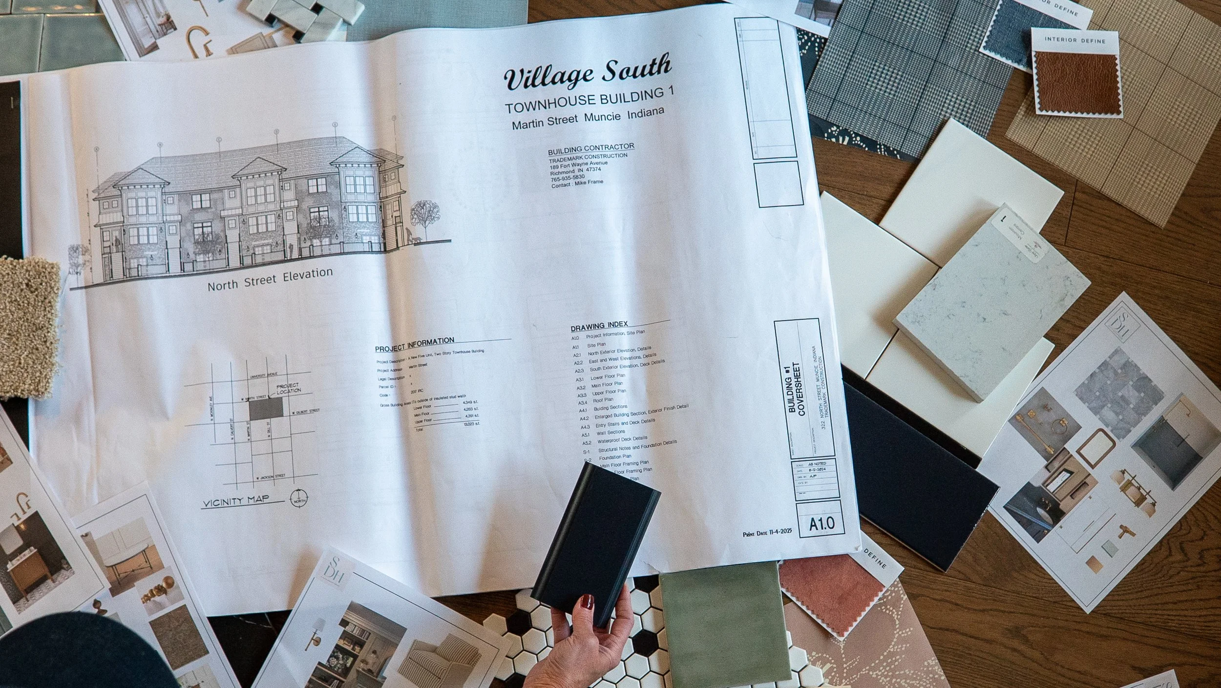 Architectural blueprint and interior design samples on a wooden table, including drawings, color swatches, and material samples for a townhouse project.