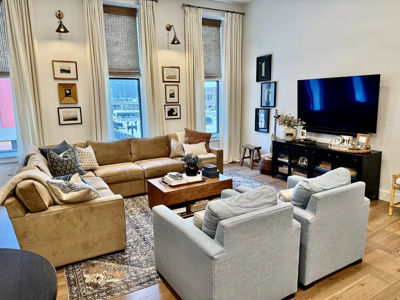 Living room with beige and gray sofas, a wooden coffee table, a television on a black stand, and framed art on the walls.