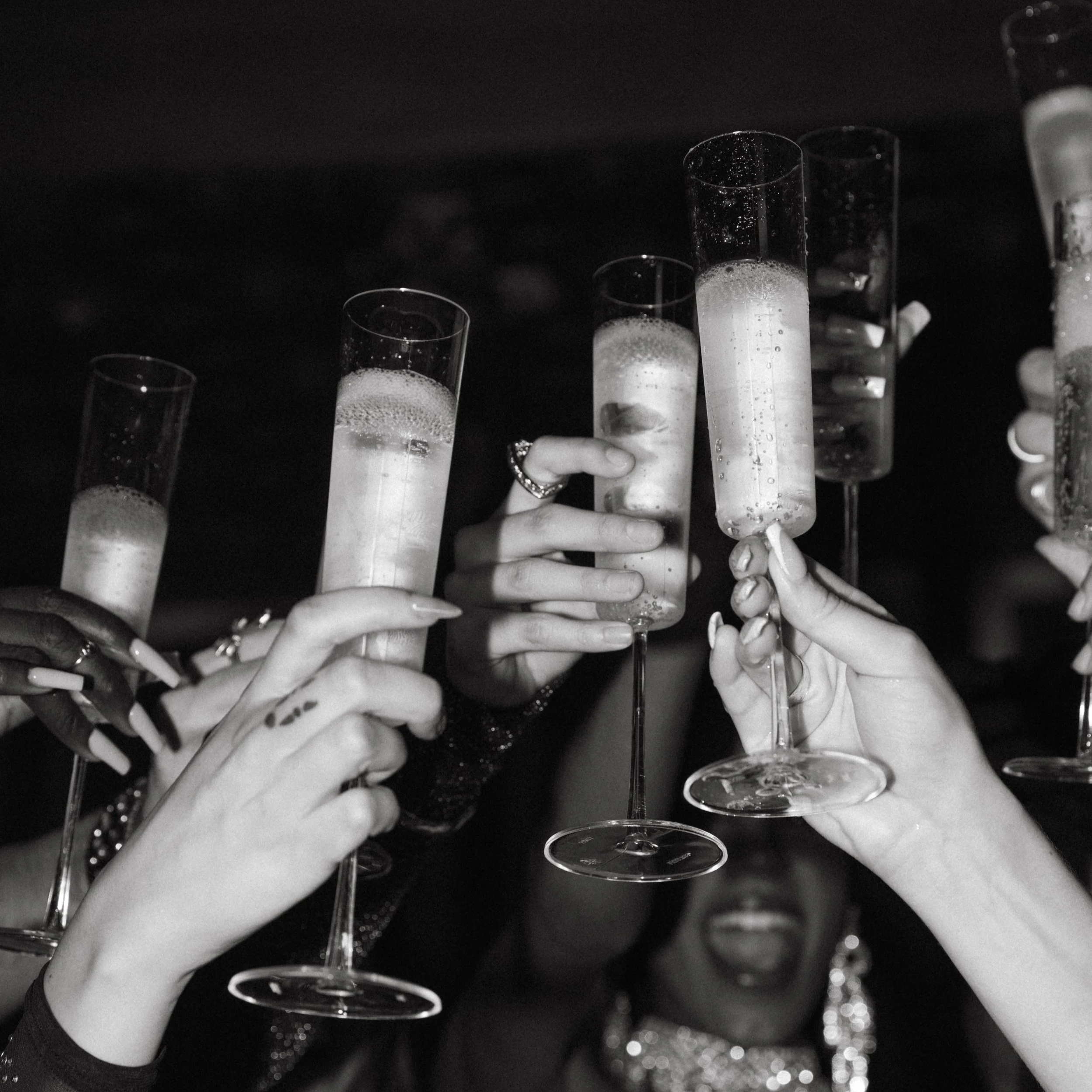 Multiple people holding champagne flutes filled with sparkling wine or champagne, toasting during a celebration.