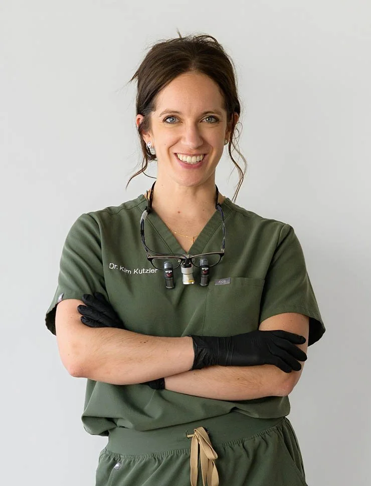 A female healthcare professional in green scrubs, smiling, standing against a white background.