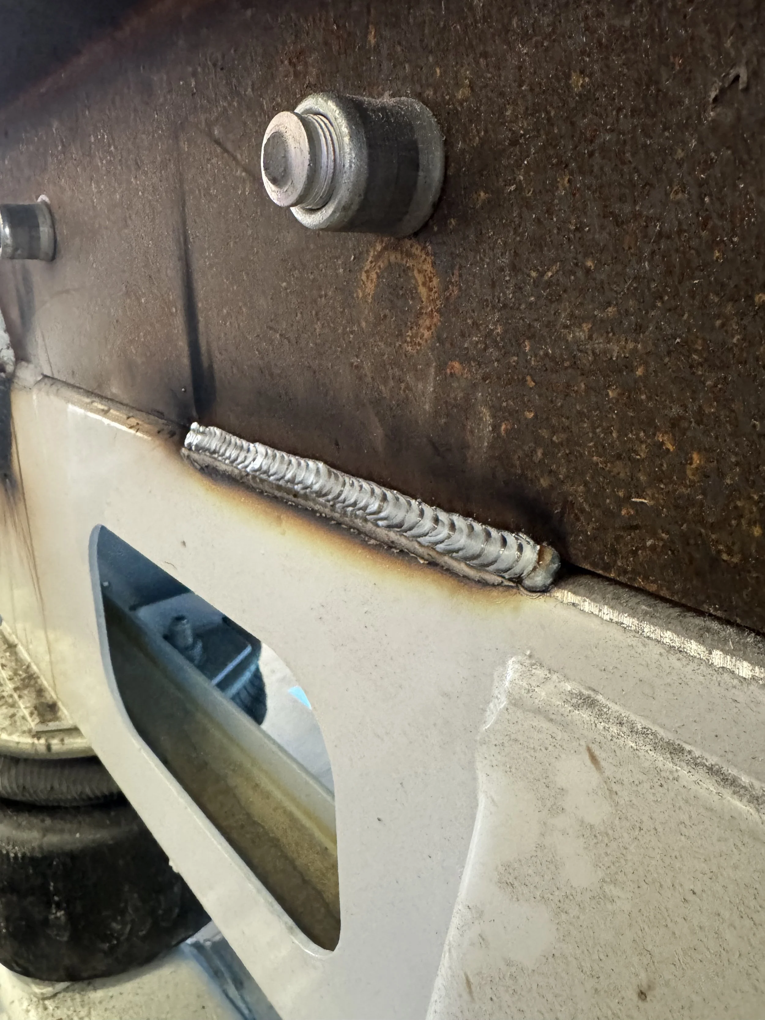 Close-up of a welded metal joint on metal surfaces, with a rusty surface above and a white painted surface below.