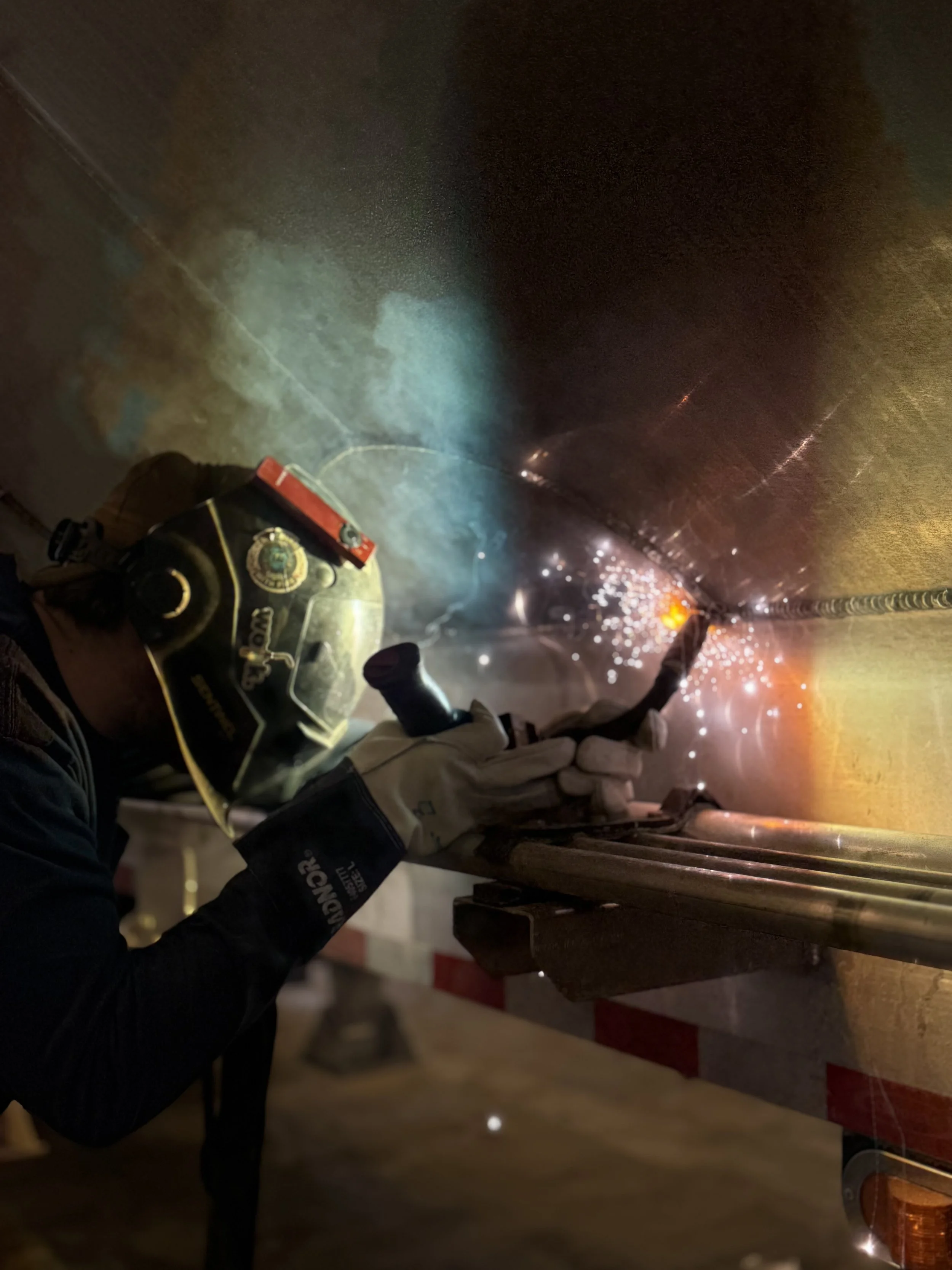 A worker using a welding torch on a metal surface, creating bright sparks and light with protective gear including a helmet and gloves.