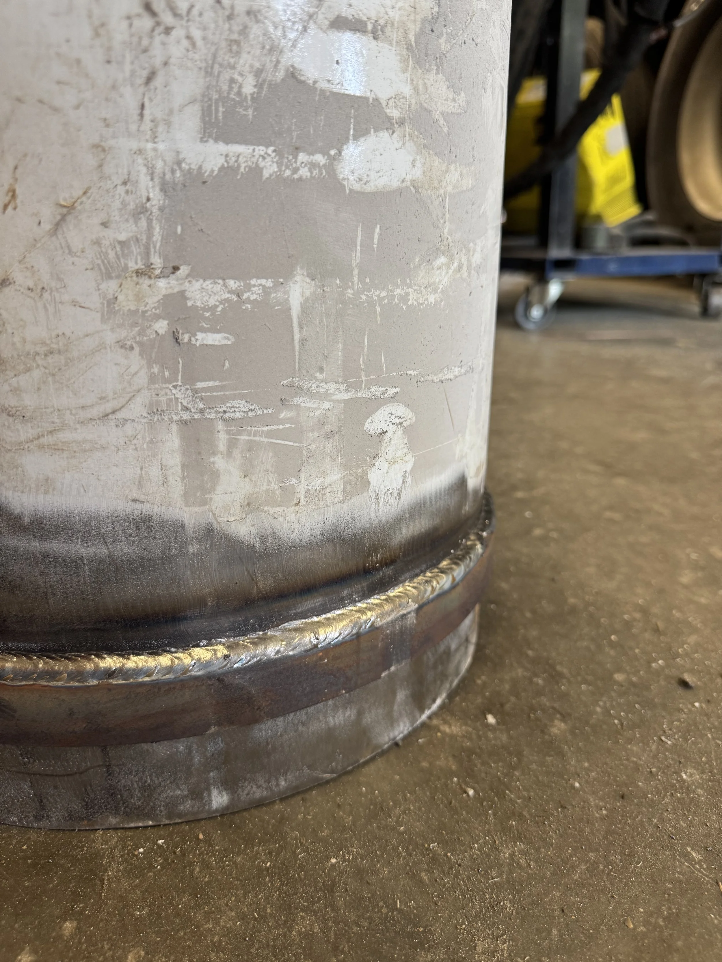 Close-up of a metal drum with welded seam, on a concrete floor in a workshop or garage.
